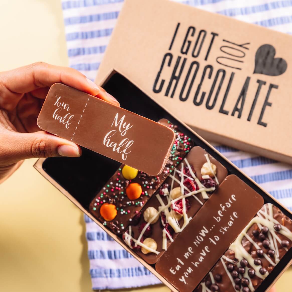 An 'I got you chocolate' branded gift box showing five handmade Belgian chocolate boxes inside. One, with a 'You half/My half' message is being held up to the camera.