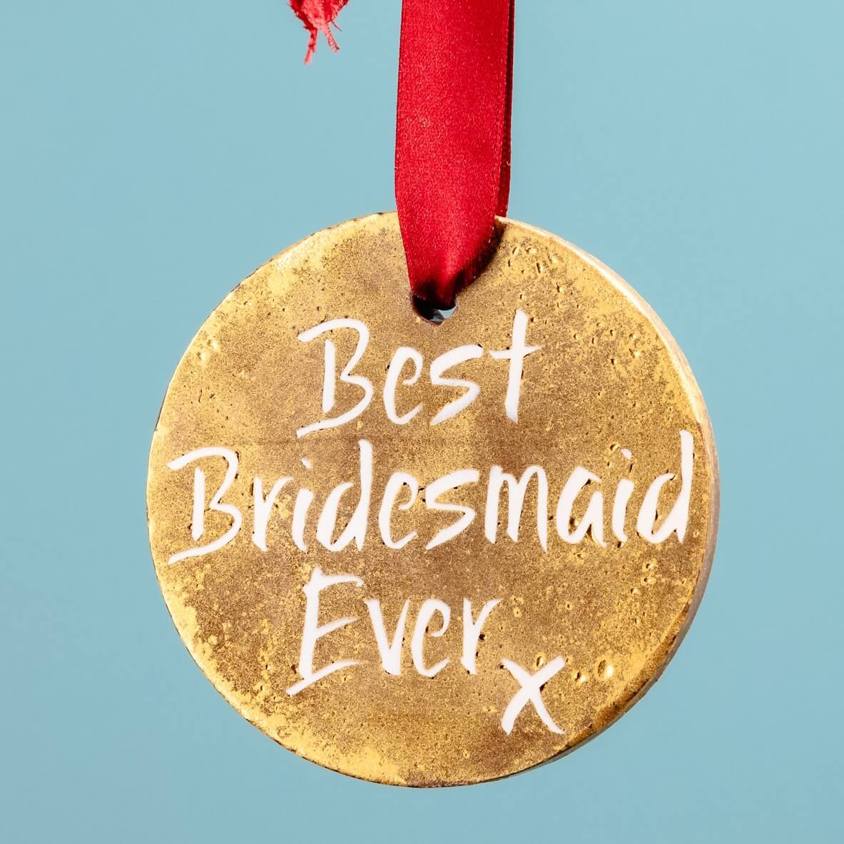 A hand holding a gold chocolate medal with a red ribbon and the message “Best Bridesmaid Ever” – a fun and edible bridesmaid chocolate gift that’s ready to wear (and eat)
