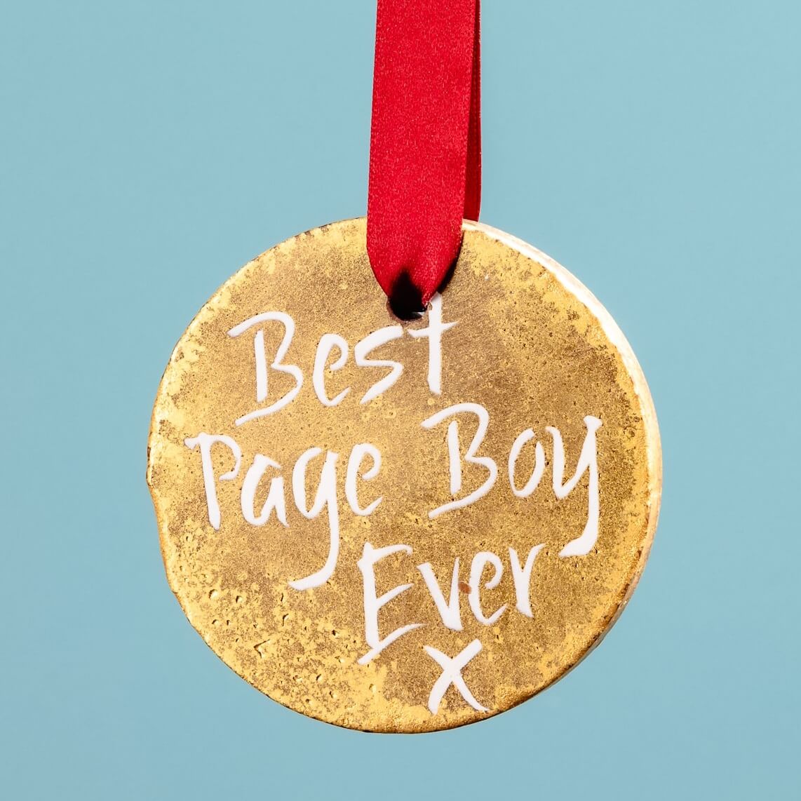 A hand holding a gold chocolate medal with a red ribbon and the words “Best Page Boy Ever” – a fun chocolate page boy gift to say thanks on the big day.