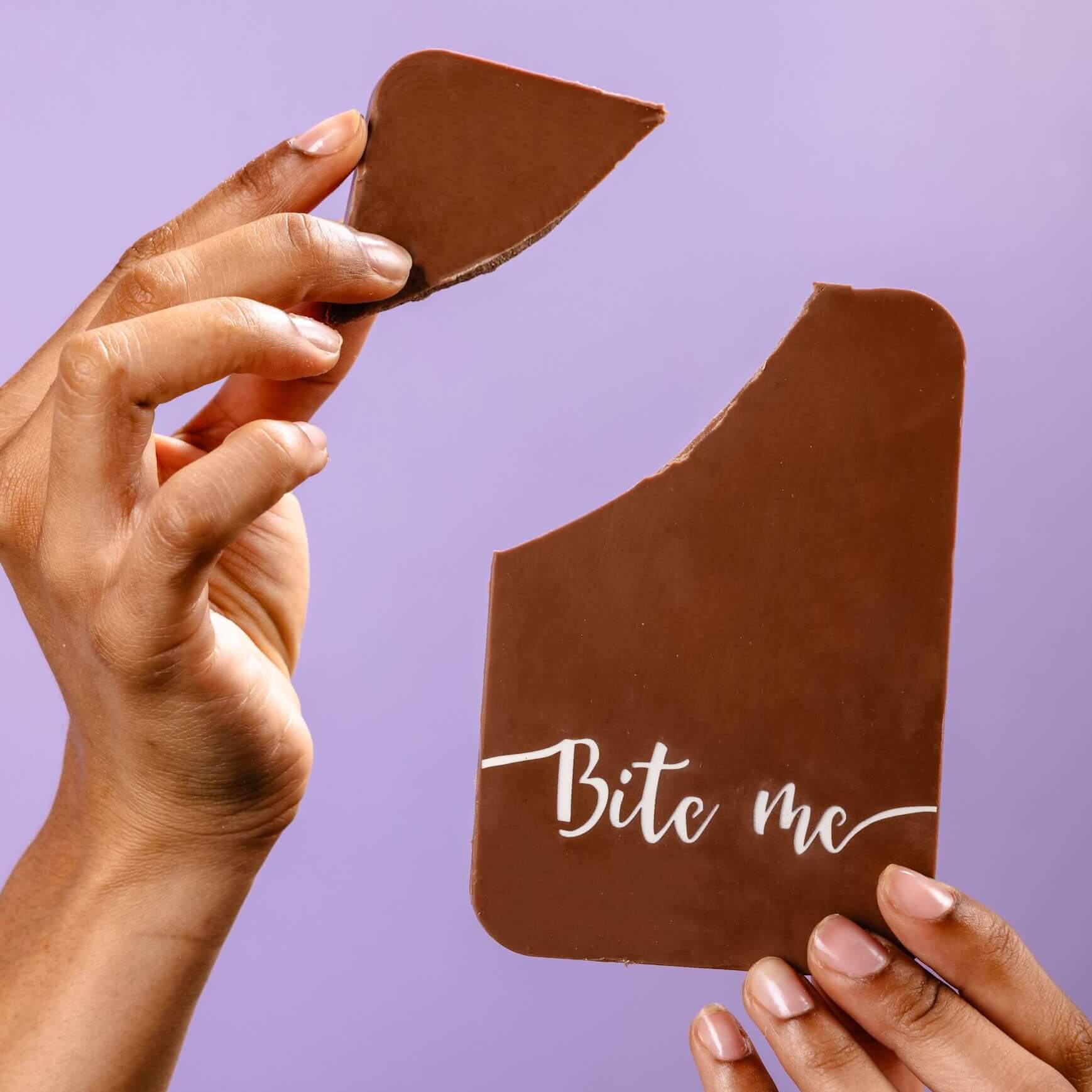Hands holding a broken milk chocolate bar with the words “Bite me” written on it – a novelty chocolate gift that says what you're thinking, but sweeter.