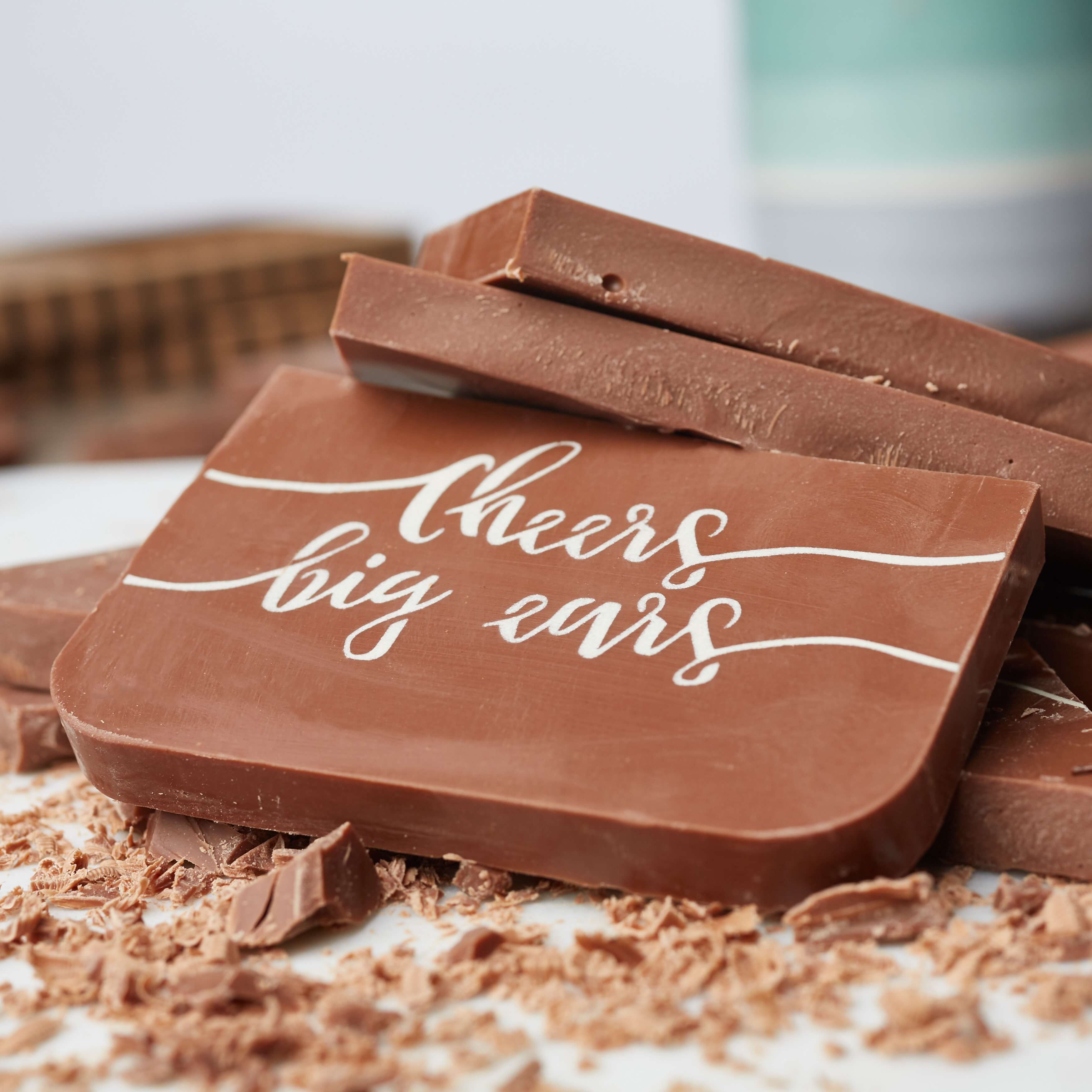 A Funny Rude Gift - Close-up of the ‘Cheers Big Ears’ chocolate bar stacked among broken pieces and shavings.