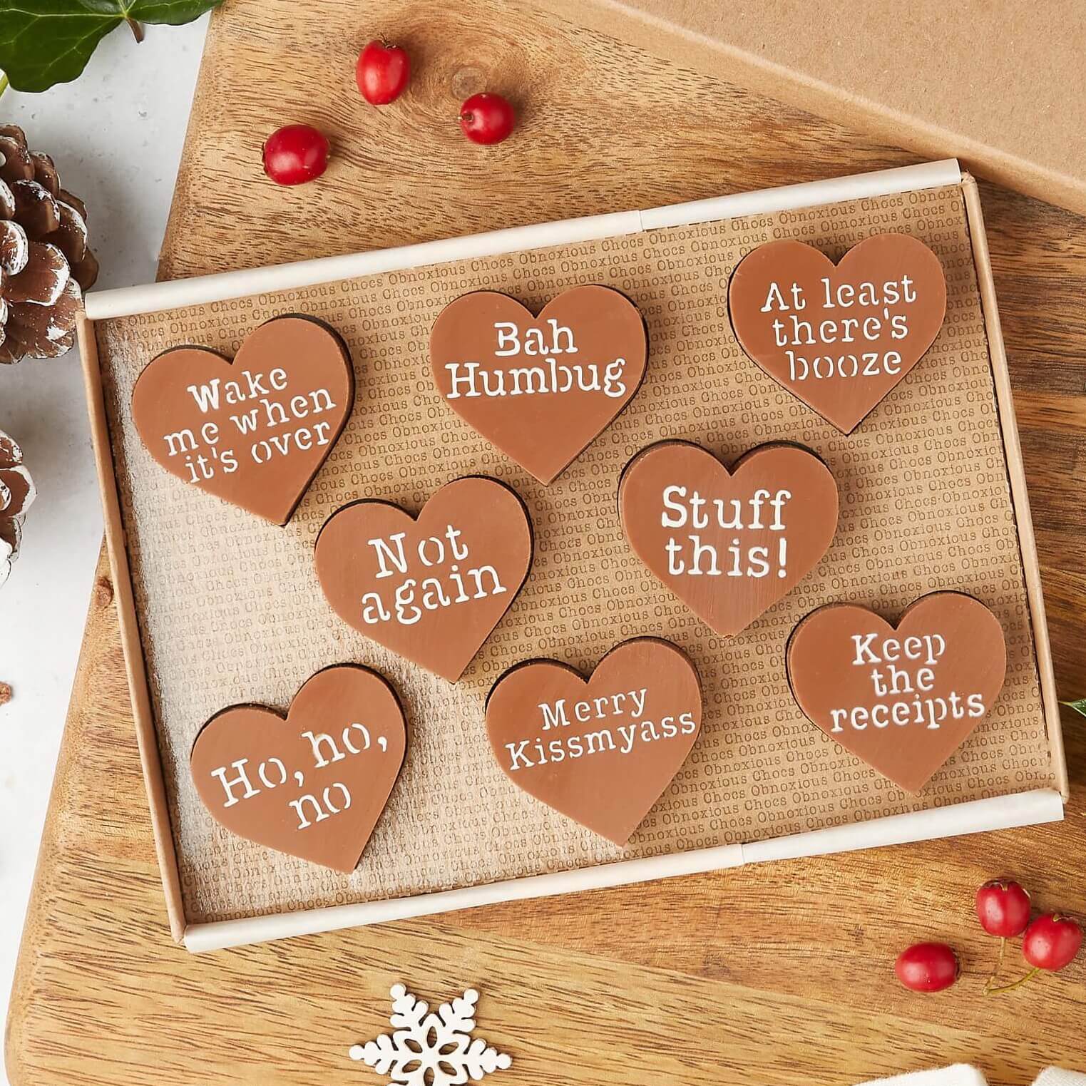 A flat-lay of heart-shaped chocolates with festively sarcastic slogans like “Merry Kissmyass” and “Keep the receipts”. Ideal chocolate for Christmas gifts with a twist of dry humour.