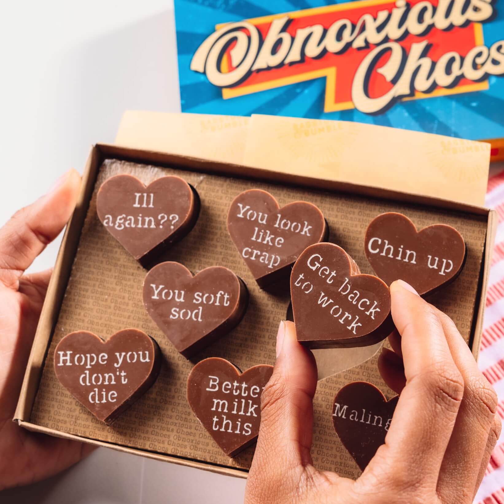 Funny Get Well Soon Gift - Hands holding a box of Bagstock & Bumble Get Well Obnoxious Chocs, packed with Belgian chocolate hearts and sarcastic get well messages.