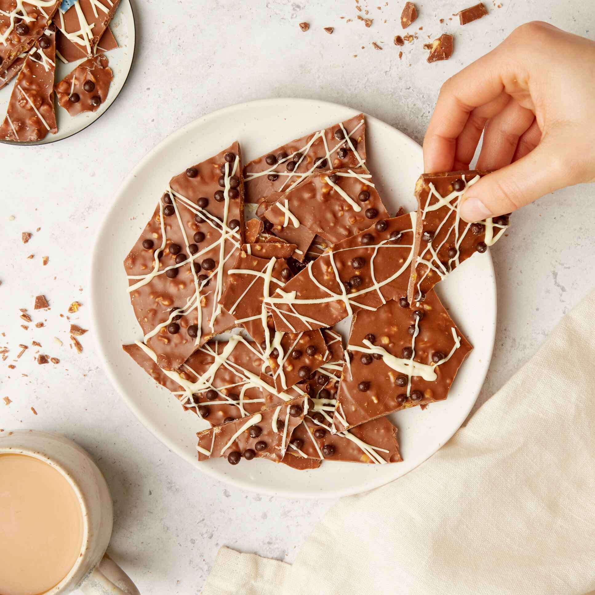 A plate piled with handmade honeycomb chocolate shards, being picked up by hand – crunchy, creamy, and unapologetically snackable.