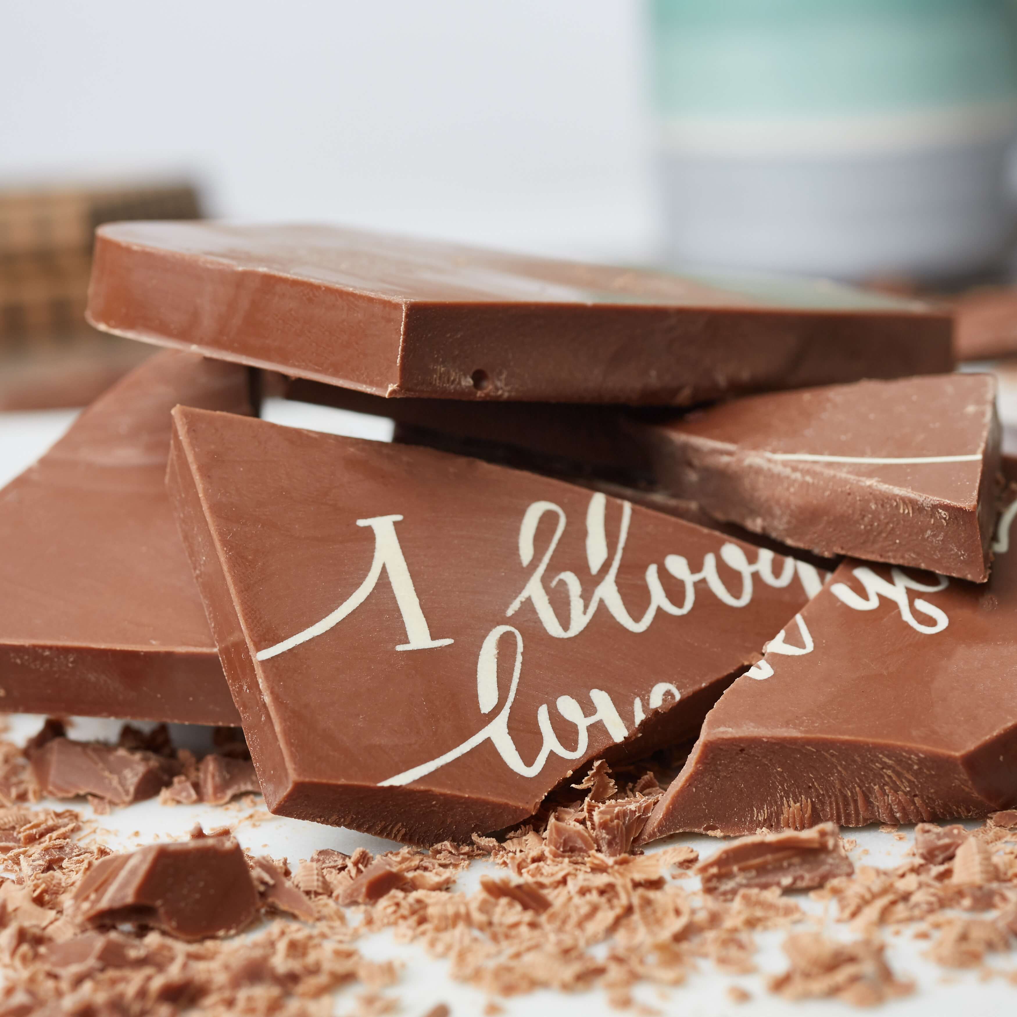 Gift ideas for best friends - Close-up of broken chunks of Belgian milk chocolate, showing the ‘I bloody love you’ message across the shards, surrounded by chocolate shavings.