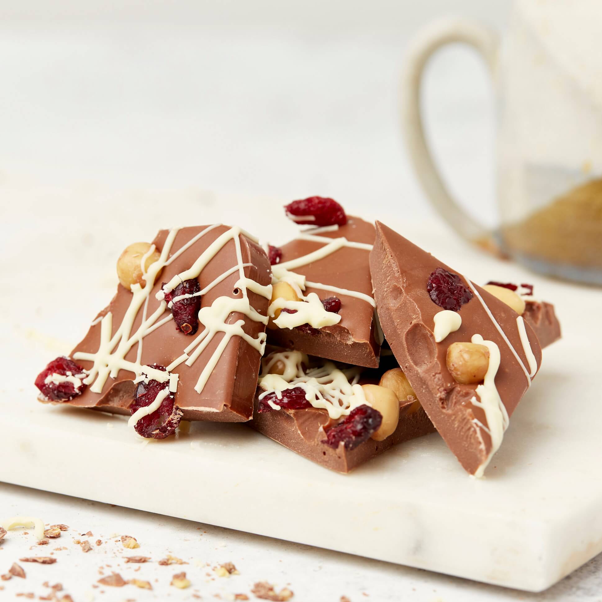 Stacked chunks of a loaded chocolate bar packed with cranberries, hazelnuts, and creamy Belgian milk chocolate, with white chocolate drizzle on top.