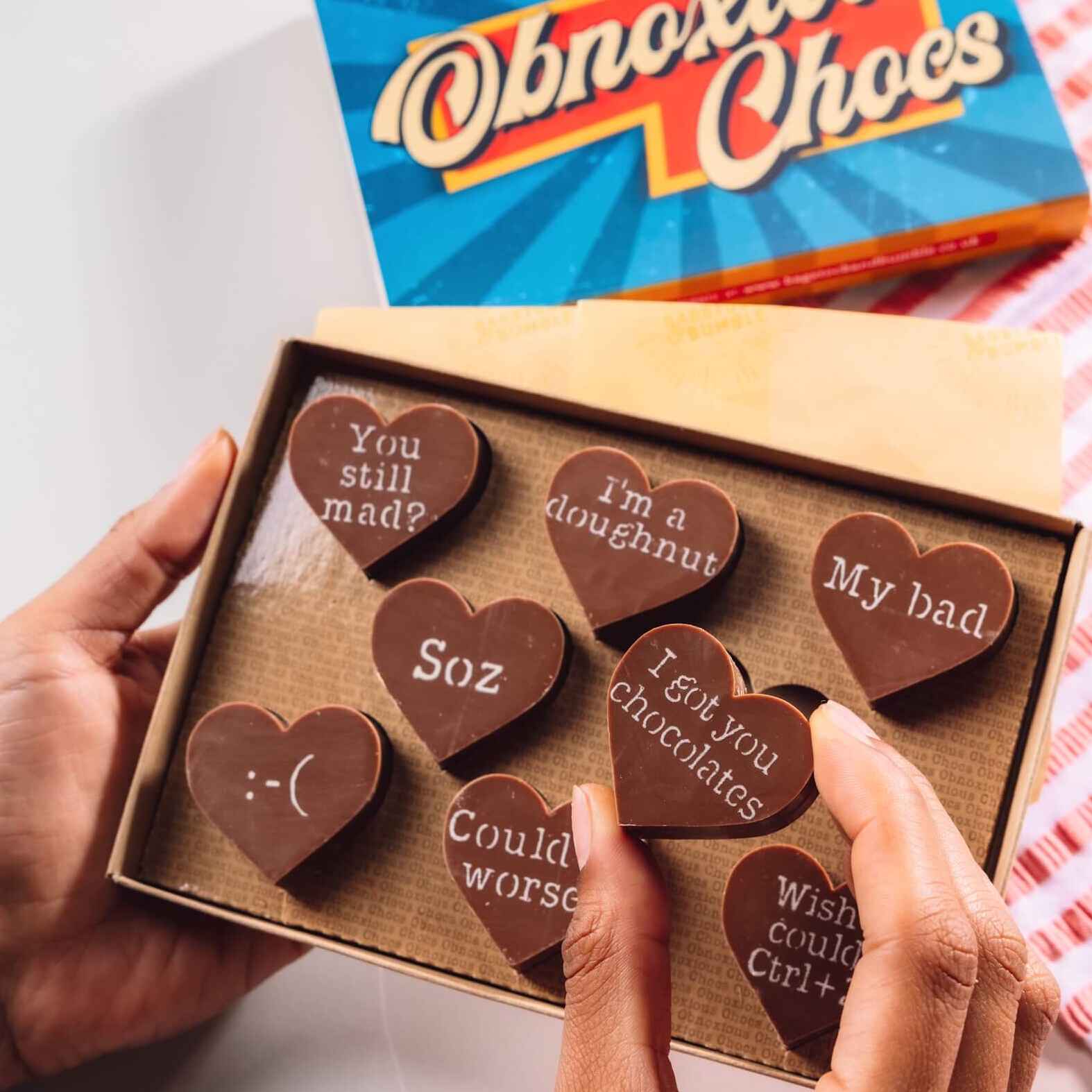 Hand holding a box of Bagstock & Bumble Sorry Obnoxious Chocs, packed with chunky Belgian chocolate hearts and sarcastic apology messages.