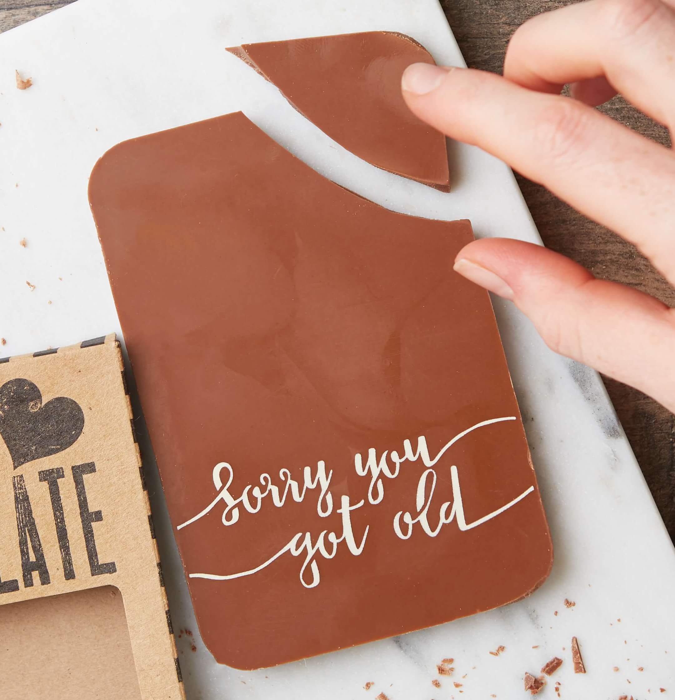 A hand breaking a chunky milk chocolate bar with the message ‘Sorry you got old’—a perfect funny chocolate gift for birthdays for someone who’s pretending not to care.