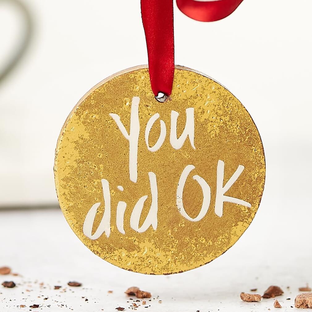 A hand holding a gold chocolate medal with a red ribbon and the words "You did OK" written on it – a light-hearted option for funny gifts for friends.