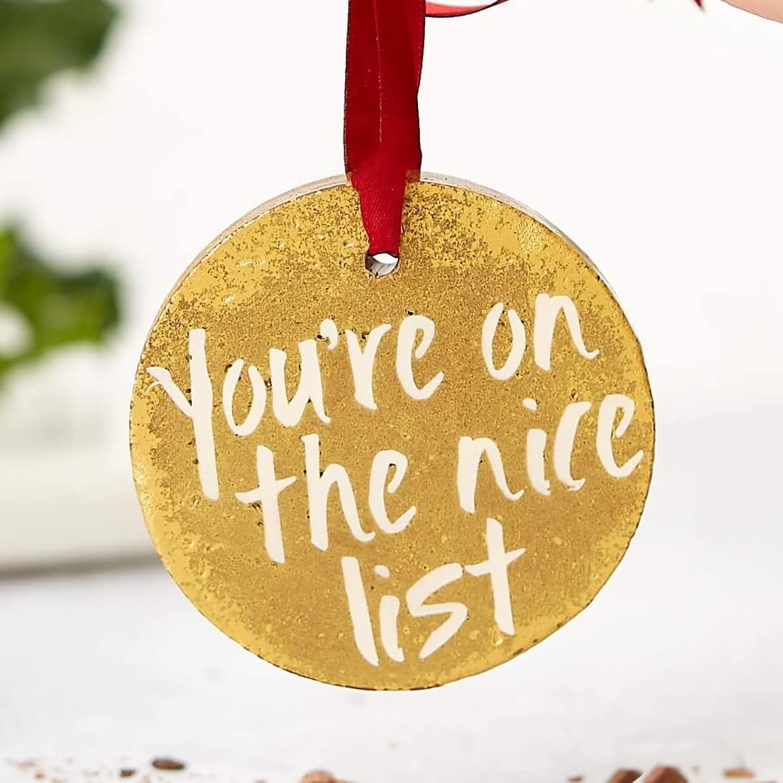 A goldmilk chocolate medal with a red ribbon and the words “You’re on the nice list”, being held up by hand. A festive treat that makes ideal chocolate stocking fillers for the good ones!