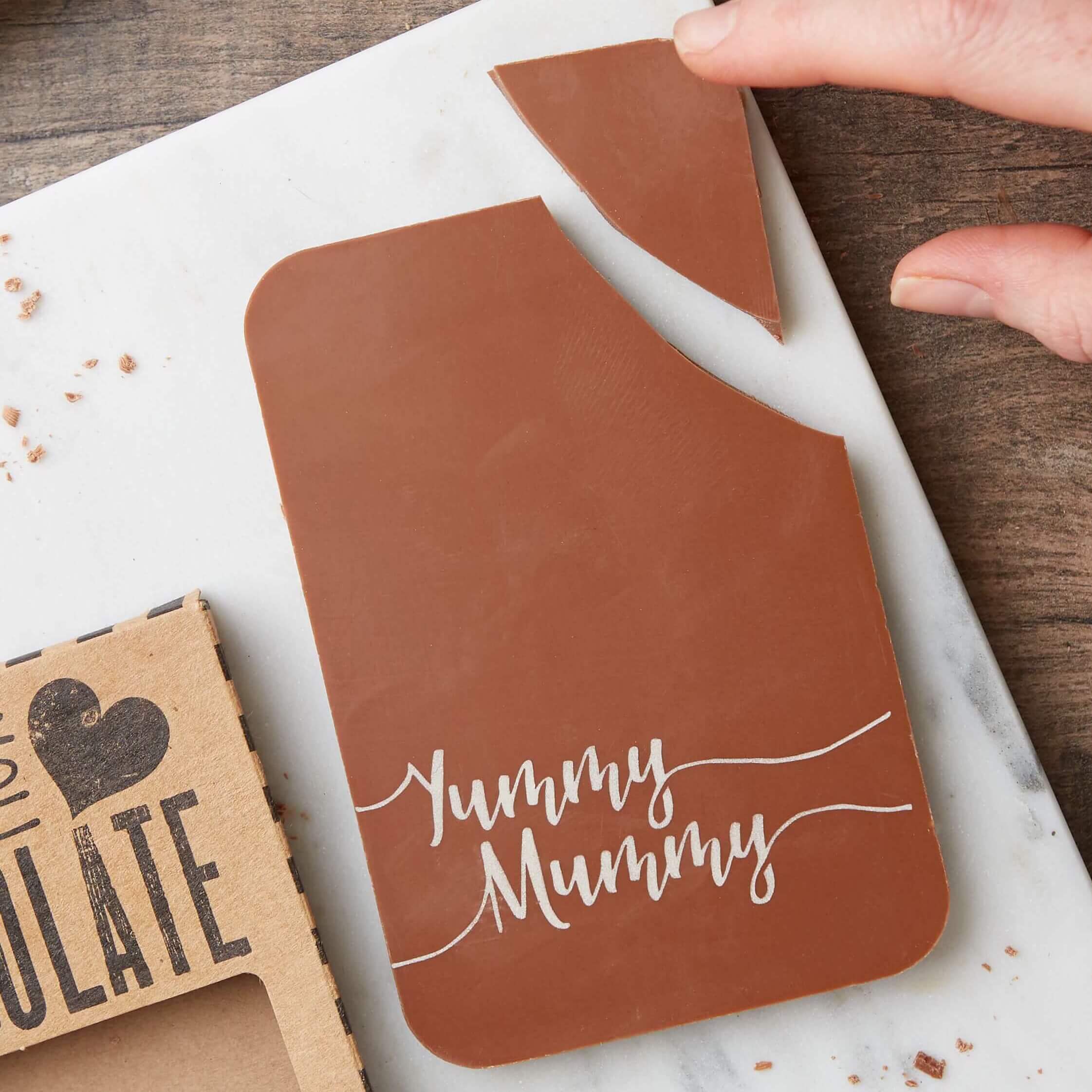 Yummy Mummy milk chocolate bar shown next to its packaging and with the corner broken off. If you're going to get your Mum chocolate, this is the chocolate you need.