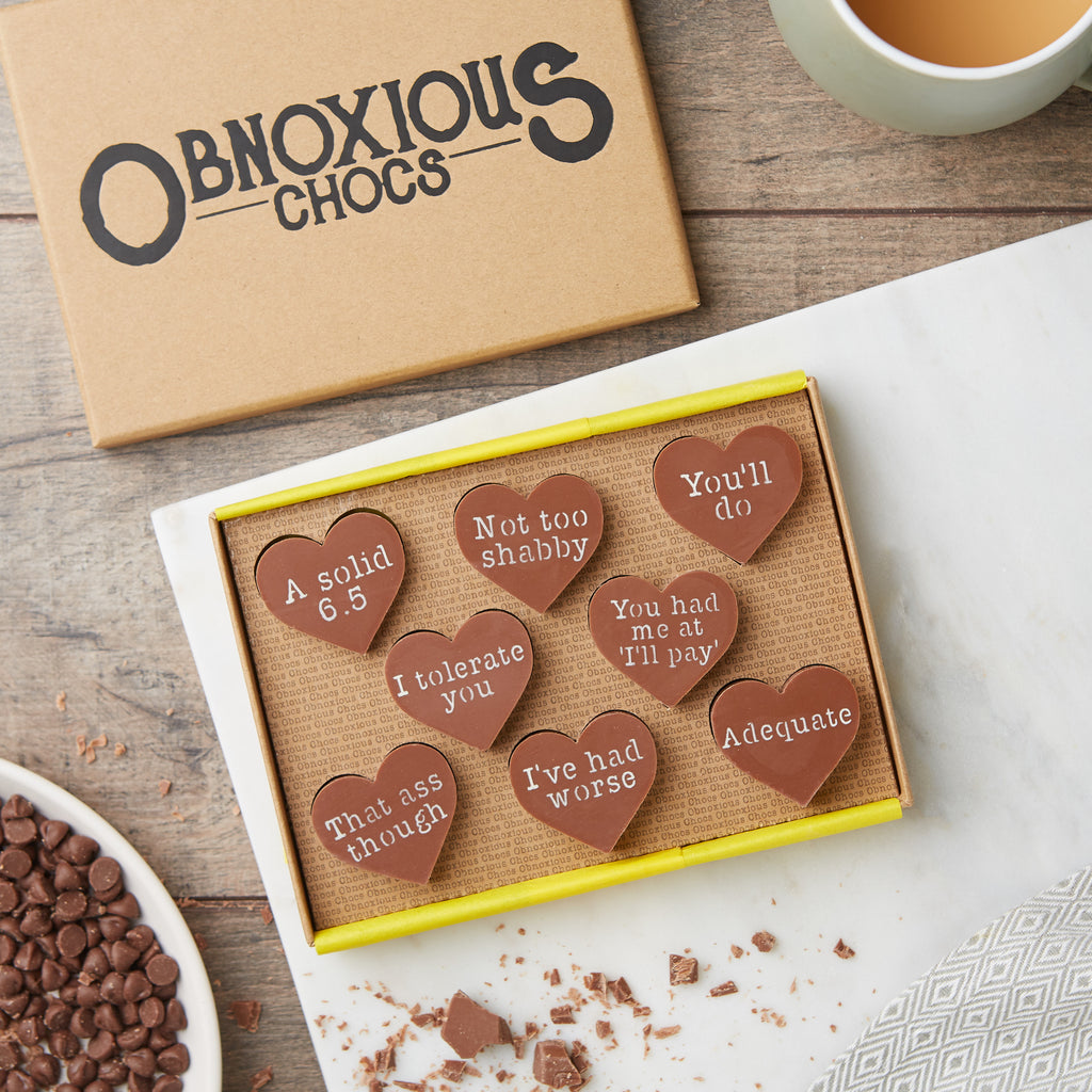 A bird's eye view of the Obnoxious Chocs gift box for partners with cheeky Valentine's messages.  The messages read:  'A solid 6.5'; Not too shabby'; 'You'll do'; 'I tolerate you'; 'You had me at I'll pay'; 'That ass though'; 'I've had worse'; and 'Adequate'.