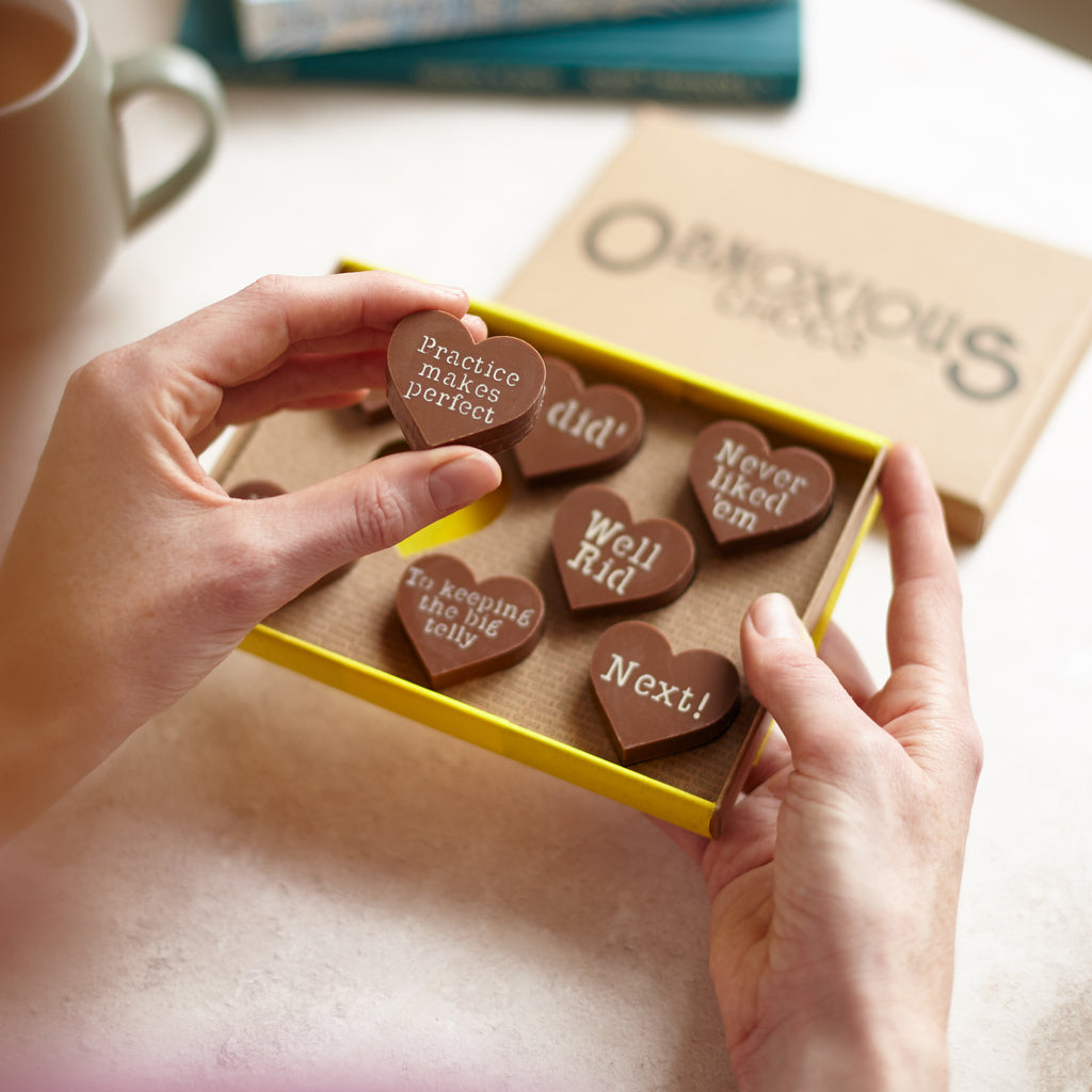 Hands holding the box of divorce themed Obnoxious Chocs, holding up a 'Practice makes perfect' milk chocolate heart