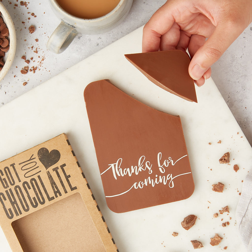 A hand coming into the frame to steal a corner of a 'Thanks for coming'  Belgian milk chocolate bar