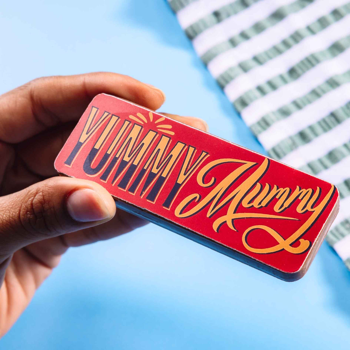 A close-up of a red and gold chocolate bar reading “Yummy Mummy” in retro-style typography. From our range of funny gifts for mum UK.