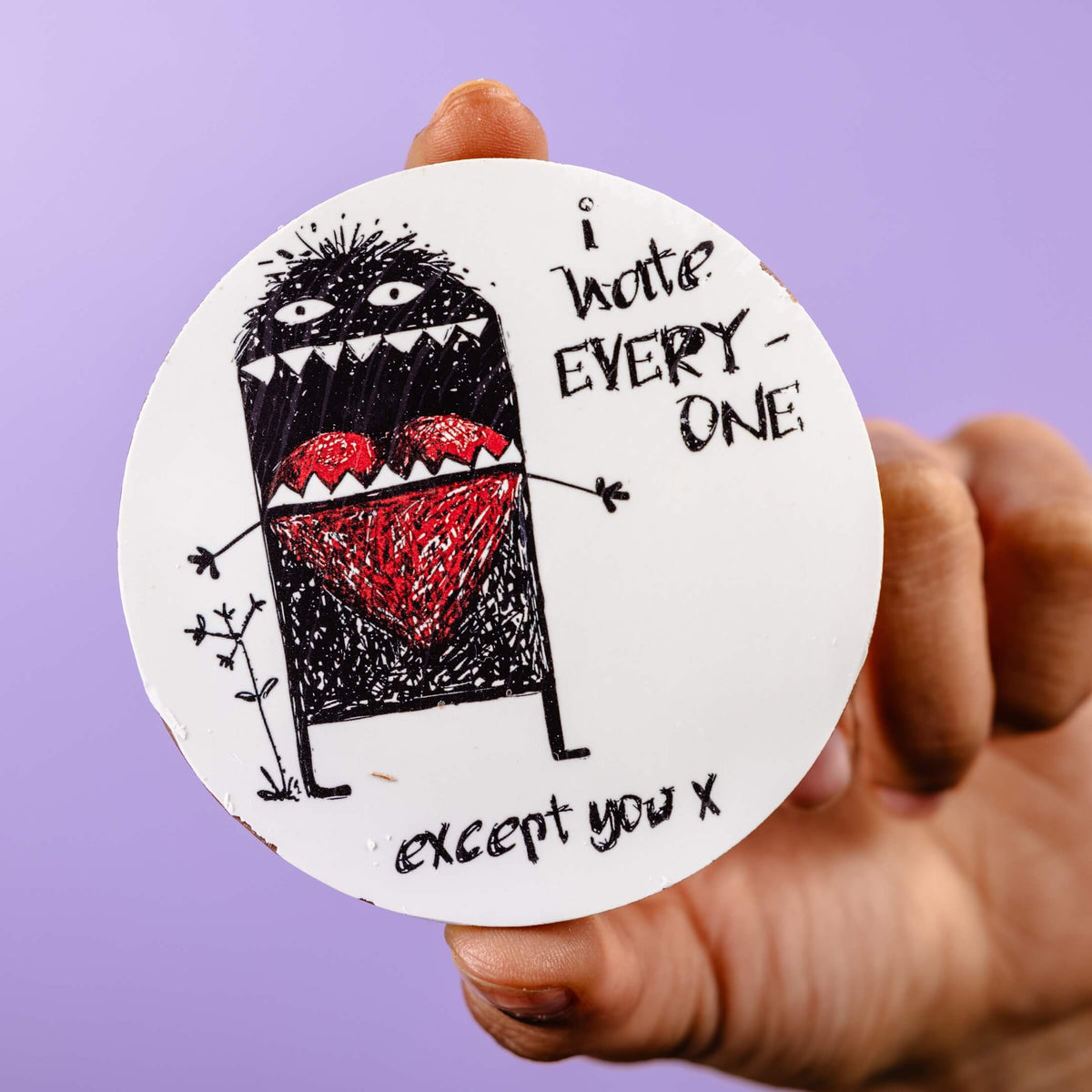 Another angle of the illustrated chocolate disc being held up, with bold hand-drawn monster and heart, perfect for those who love a bit of heartfelt sarcasm.
