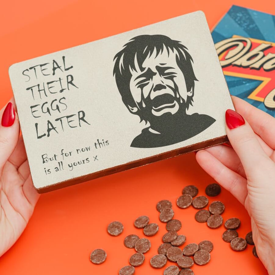 Hands holding a chunky milk chocolate slab with a crying child image and a tongue-in-cheek “Steal their eggs later” message – a bold alternative Easter chocolate for adults.