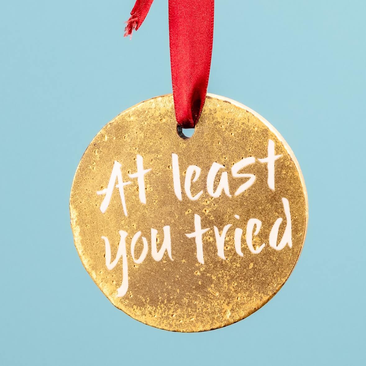 A hand holding a gold chocolate medal with a red ribbon and the words “At least you tried” – a brilliantly deadpan sarcastic congratulations gift for when it's the effort that counts.
