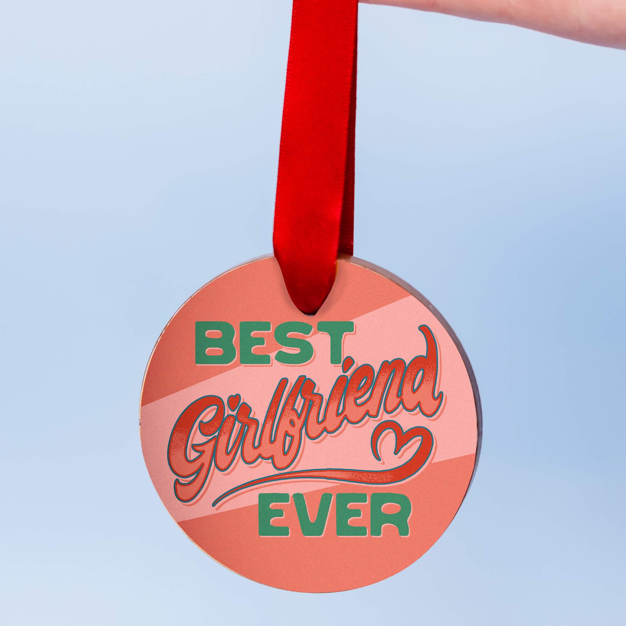 Girlfriend gifts for valentines, a chunky milk chocolate medal with a colourful edible transfer reading “Best Girlfriend Ever”, hanging from a red ribbon against a pale blue background.
