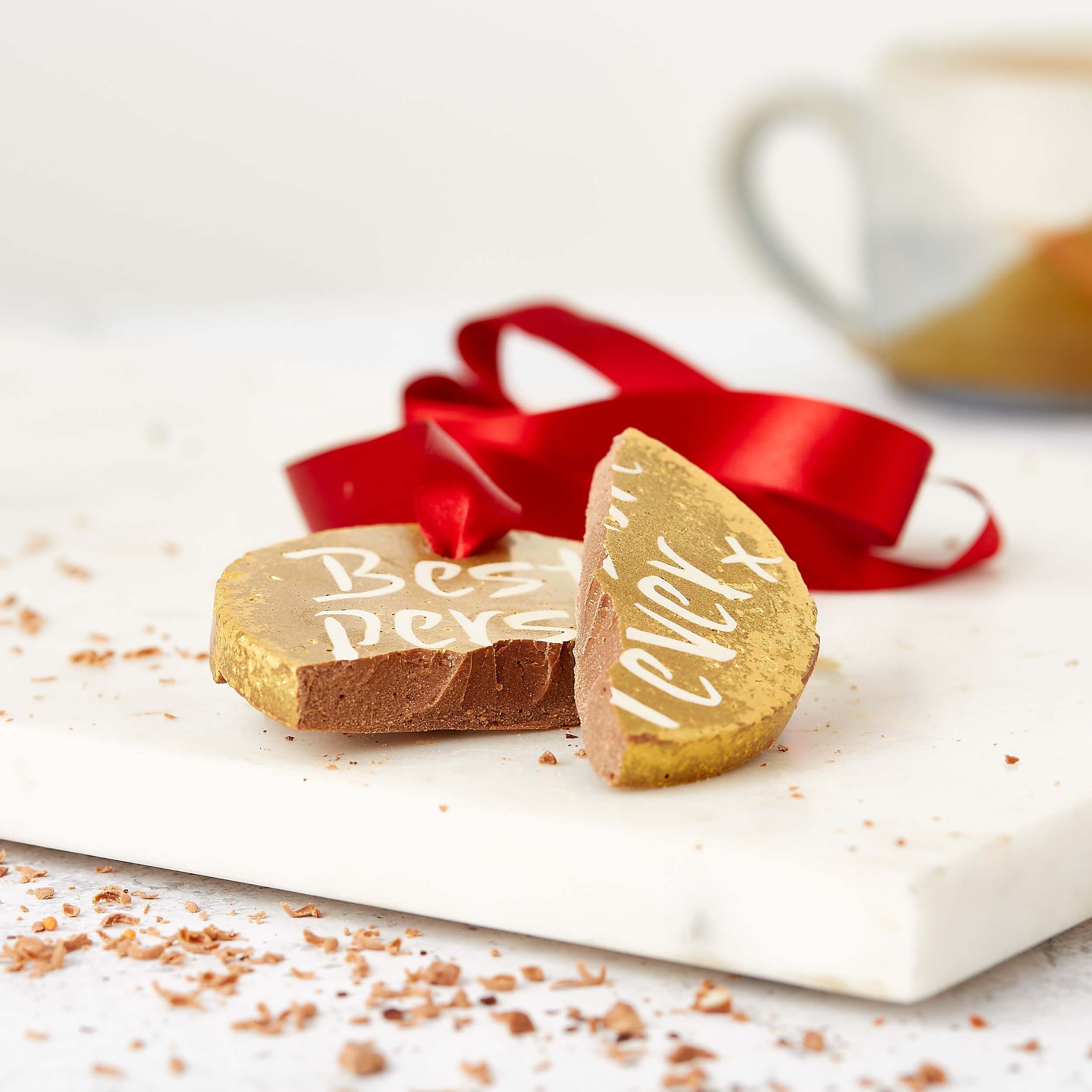 Broken chocolate medal with “Best Person Ever” showing on the pieces with its red ribbon in the background. 
 Delicious presents for friends that are made for munching.