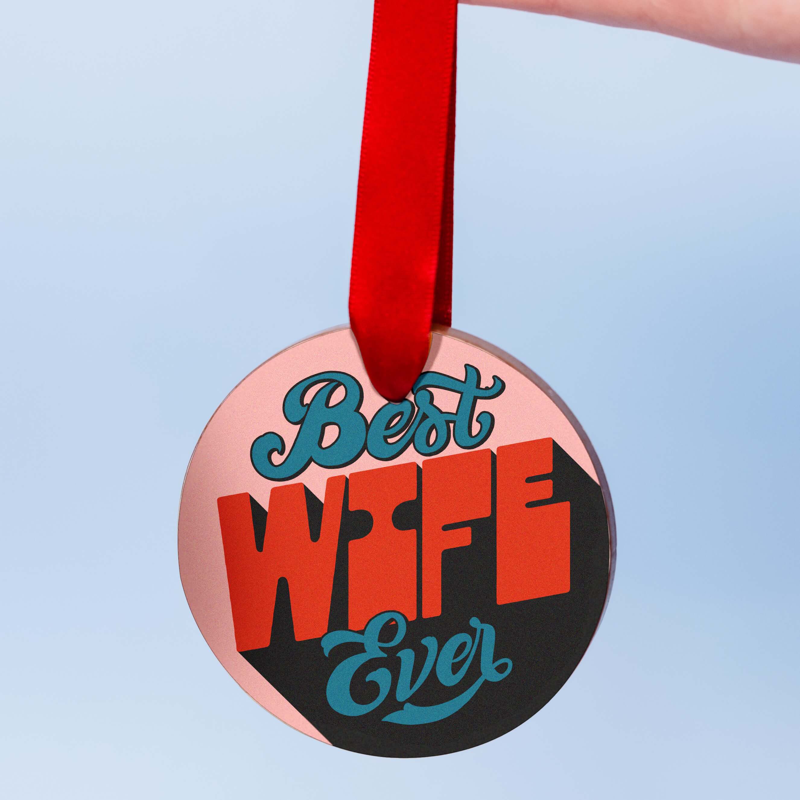Wife chocolate for valentines, a chunky milk chocolate medal with a colourful edible transfer reading “Best Wife Ever”, hanging from a red ribbon against a pale blue background.