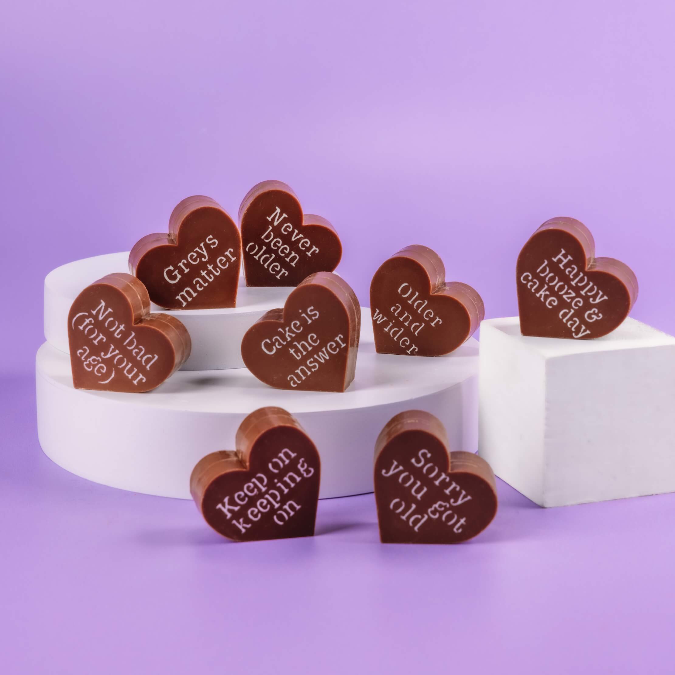 Selection of Bagstock & Bumble happy birthday chocolate hearts displayed on plinths, showing off funny engraved messages like 'Sorry you got old', perfect for a cheeky birthday treat.