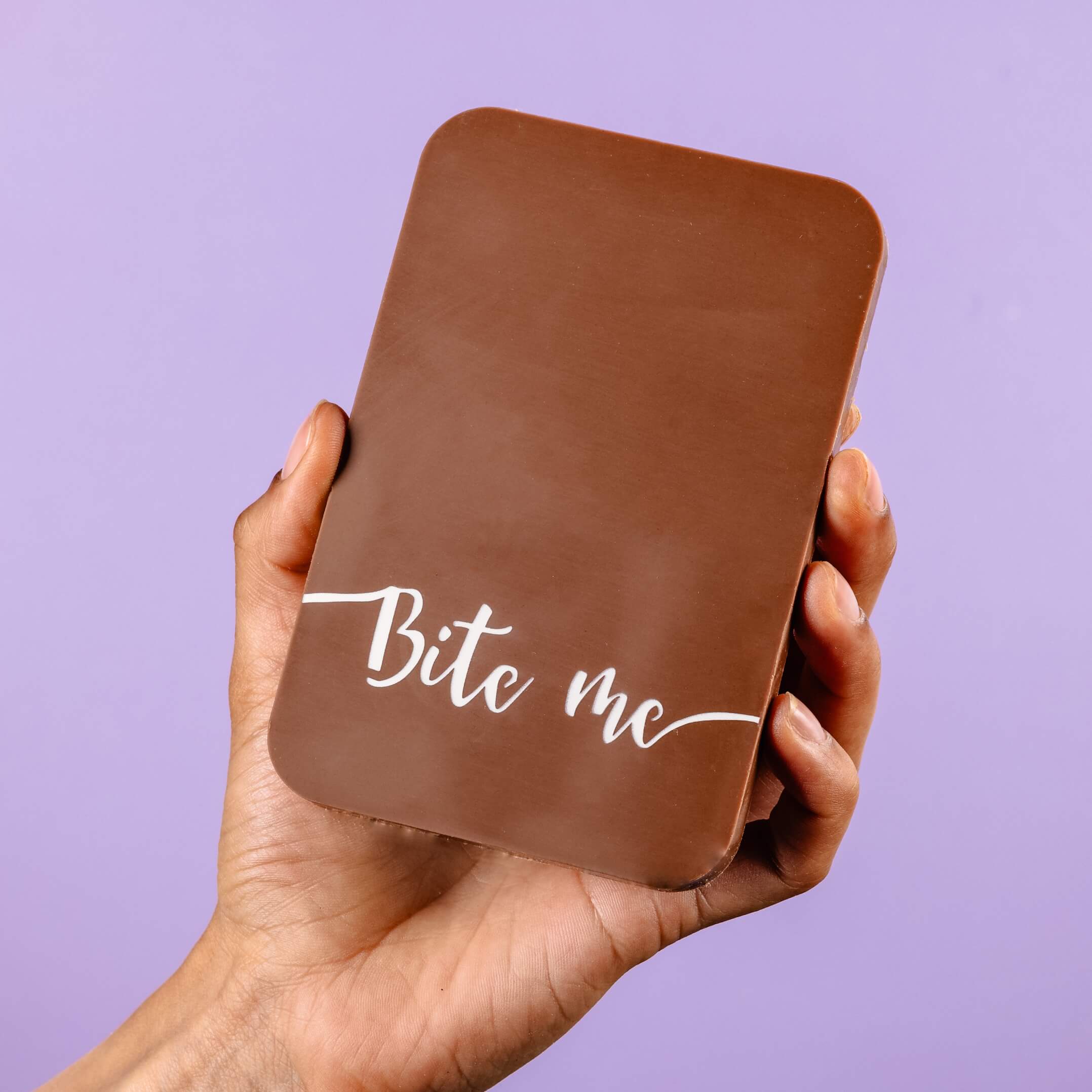 Hand holding a handmade cheeky milk chocolate bar with “Bite me” written in white script - not subtle, but still delicious.