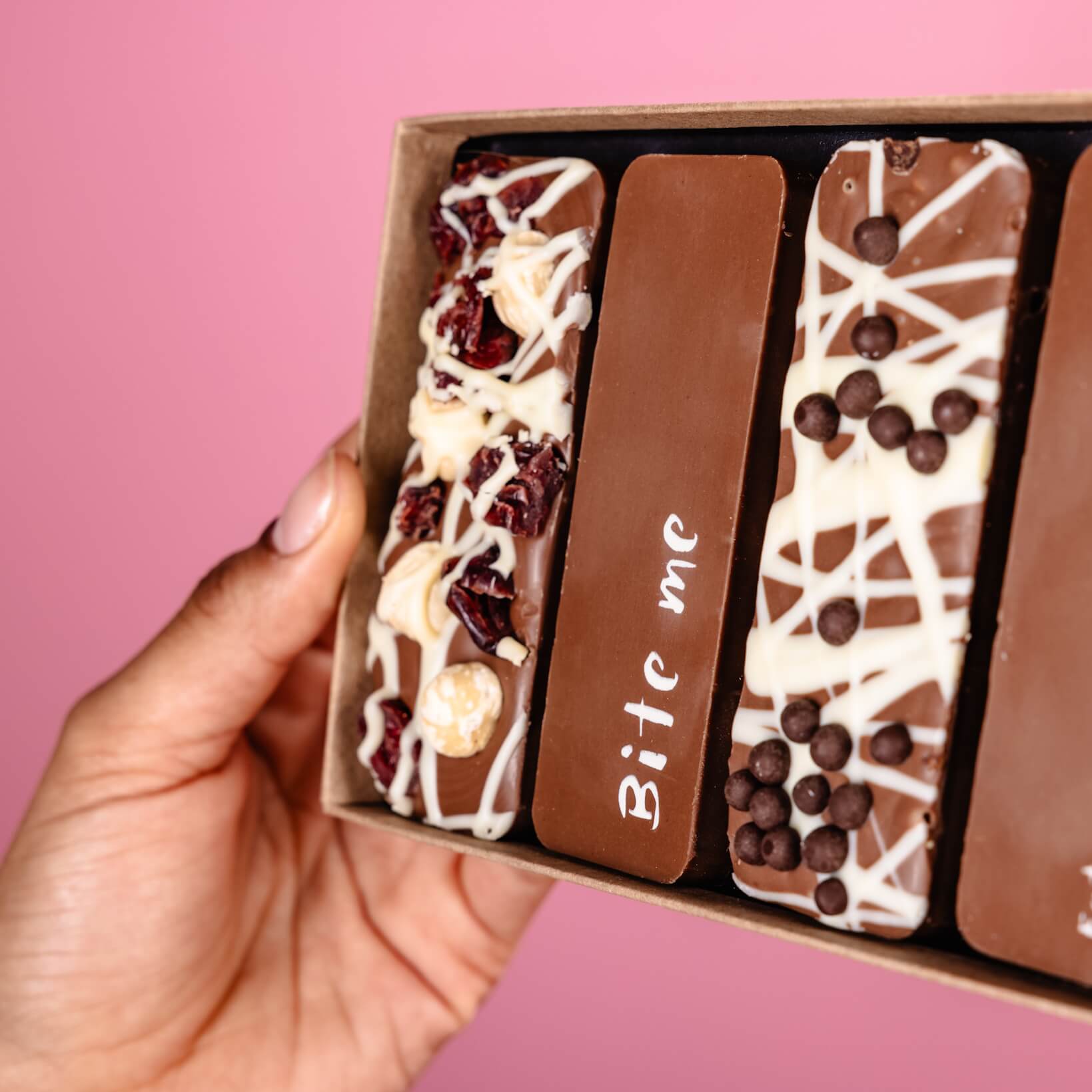 A close up of the contents of the 'I got you chocolate' Belgian chocolate selection box.   You can see a hand holding the base of the box with fruit and nut, honeycomb and 'Bite me' chocolate bars visible.