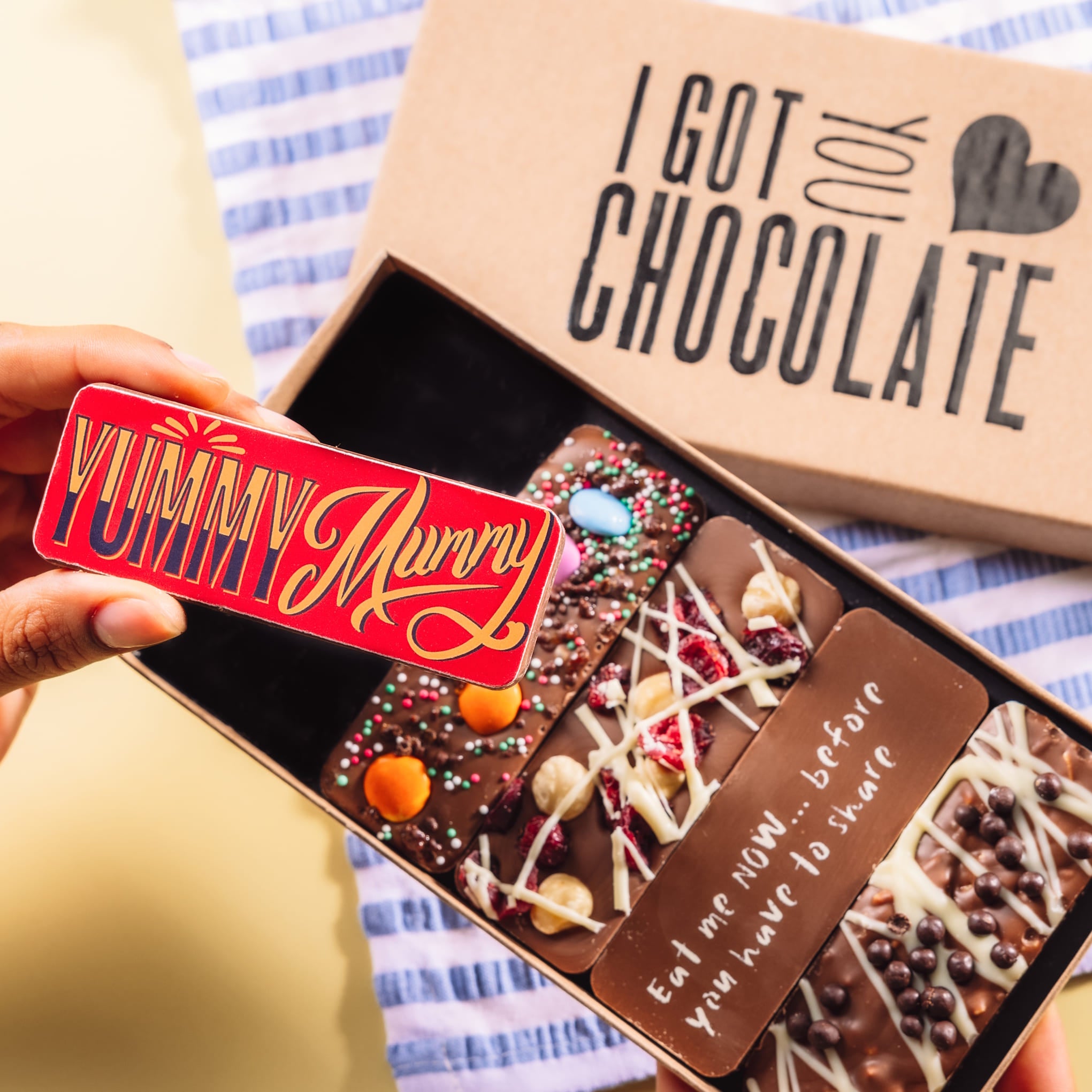 A hand holding a colourful “Yummy Mummy” chocolate bar from Bagstock & Bumble’s “I Got You Chocolate” box. Includes five handmade Belgian chocolate bars—perfect mum chocolate gifts with taste.