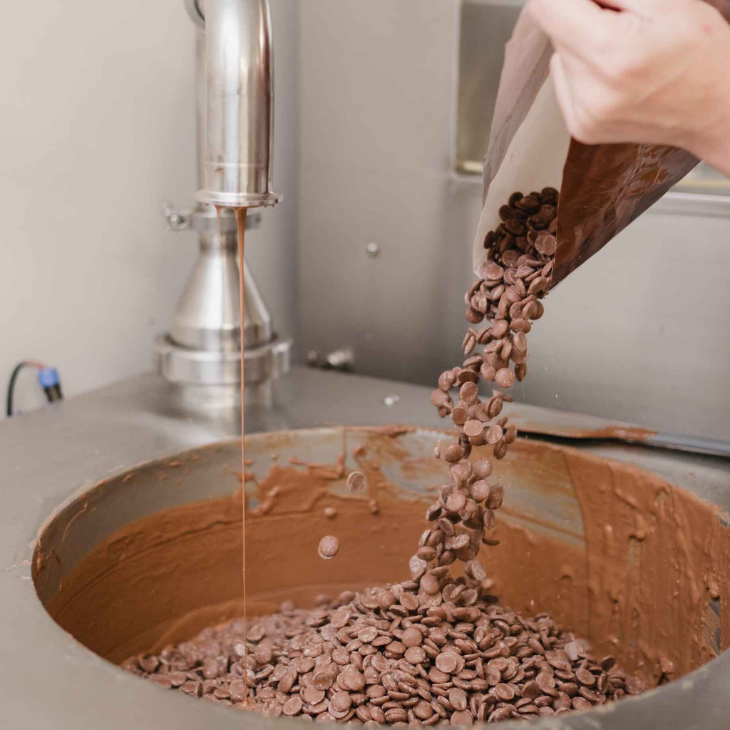 Chocolate chips being poured into a large chocolate tempering machine
