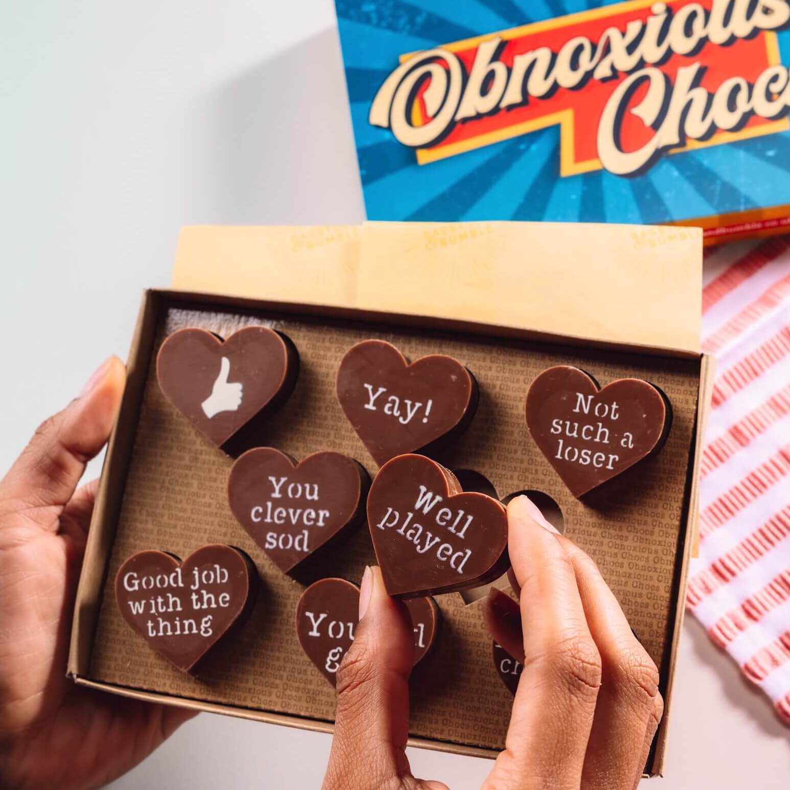 Hands holding a box of Bagstock & Bumble Congratulations Obnoxious Chocs, packed with Belgian chocolate hearts and sarcastic messages.