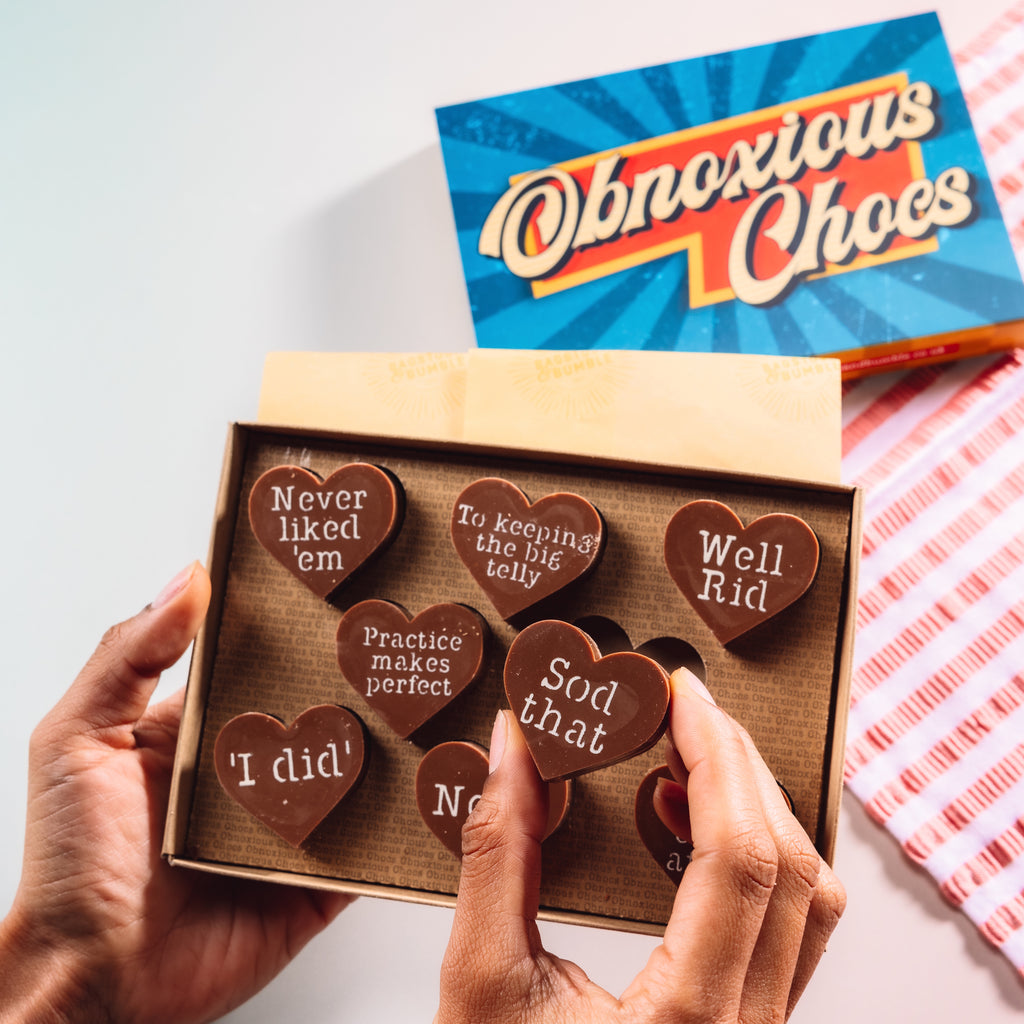 Hands holding a box of Bagstock & Bumble Divorce Obnoxious Chocs, packed with heart-shaped Fairtrade chocolates featuring cheeky post-breakup messages.