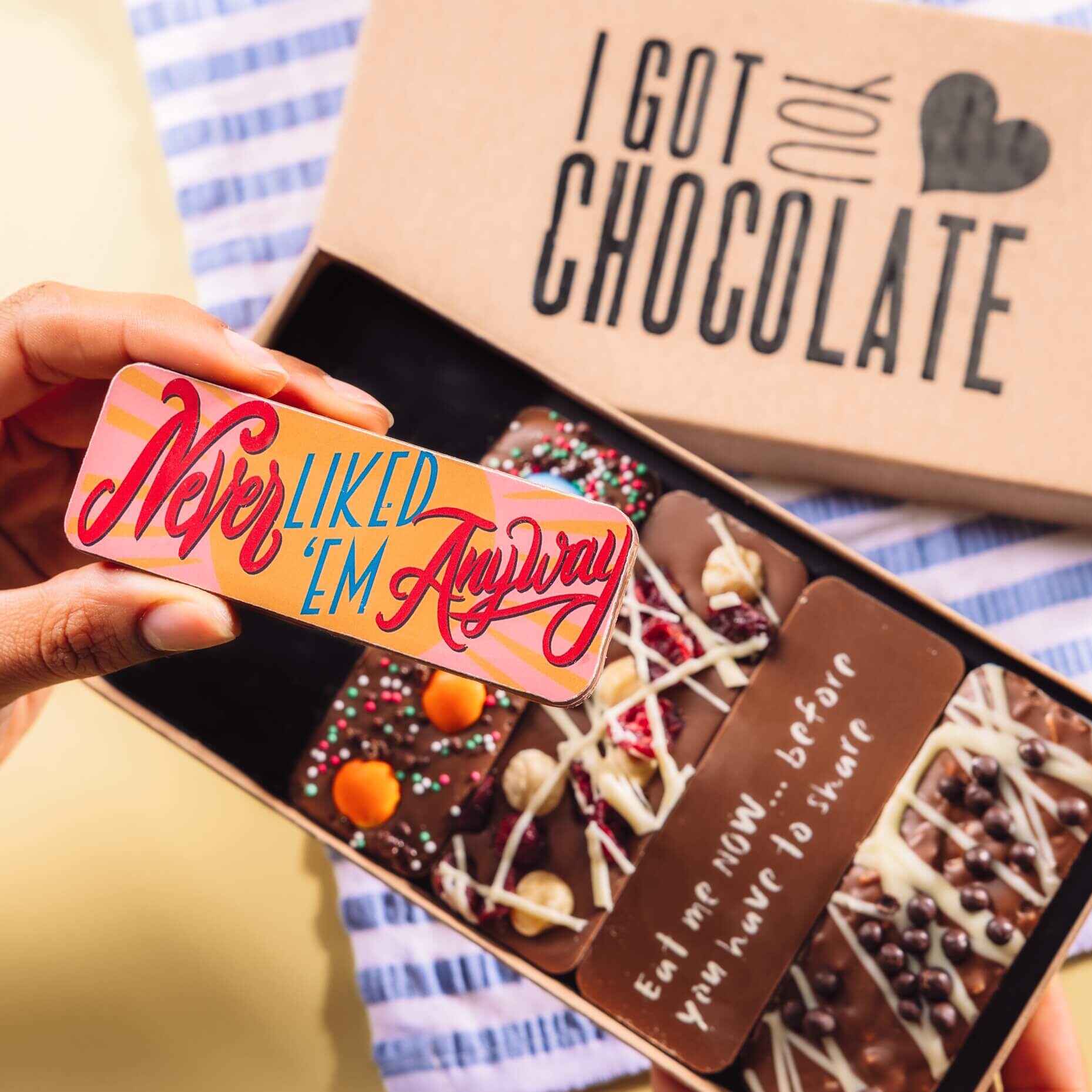 Hand holding a colourful chocolate bar that says “Never Liked ’Em Anyway”, with the rest of the 'I Got You Chocolate' gift box in the background.  A thoughtful and tasty option for divorce gifts for her.