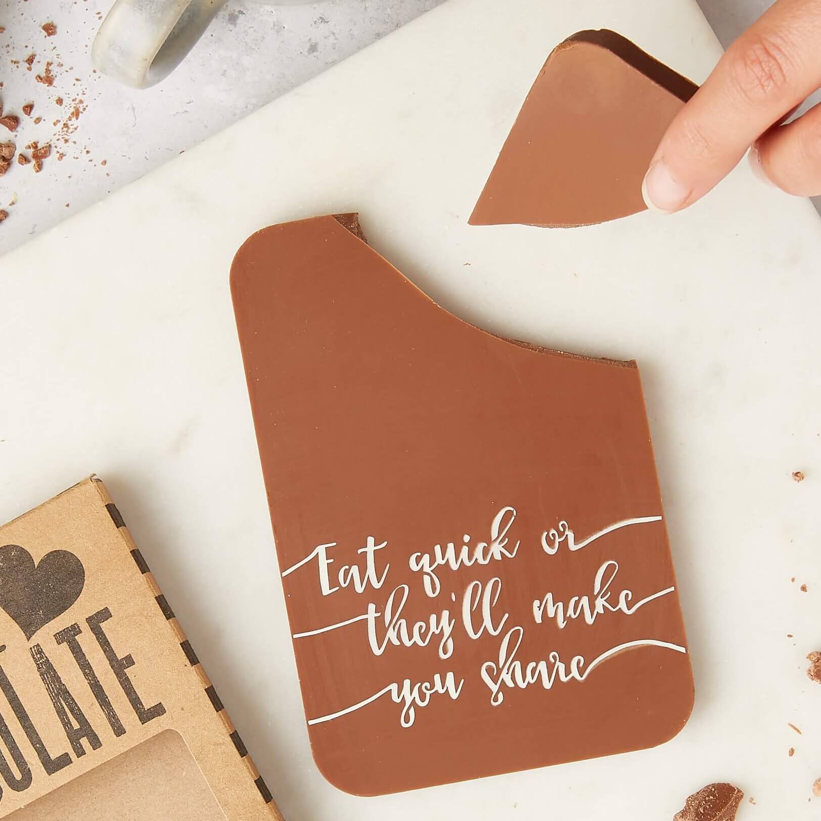 A hand breaking a piece off a milk chocolate bar that reads “Eat quick or they’ll make you share” – a unique chocolate gift for anyone who doesn’t do sharing.