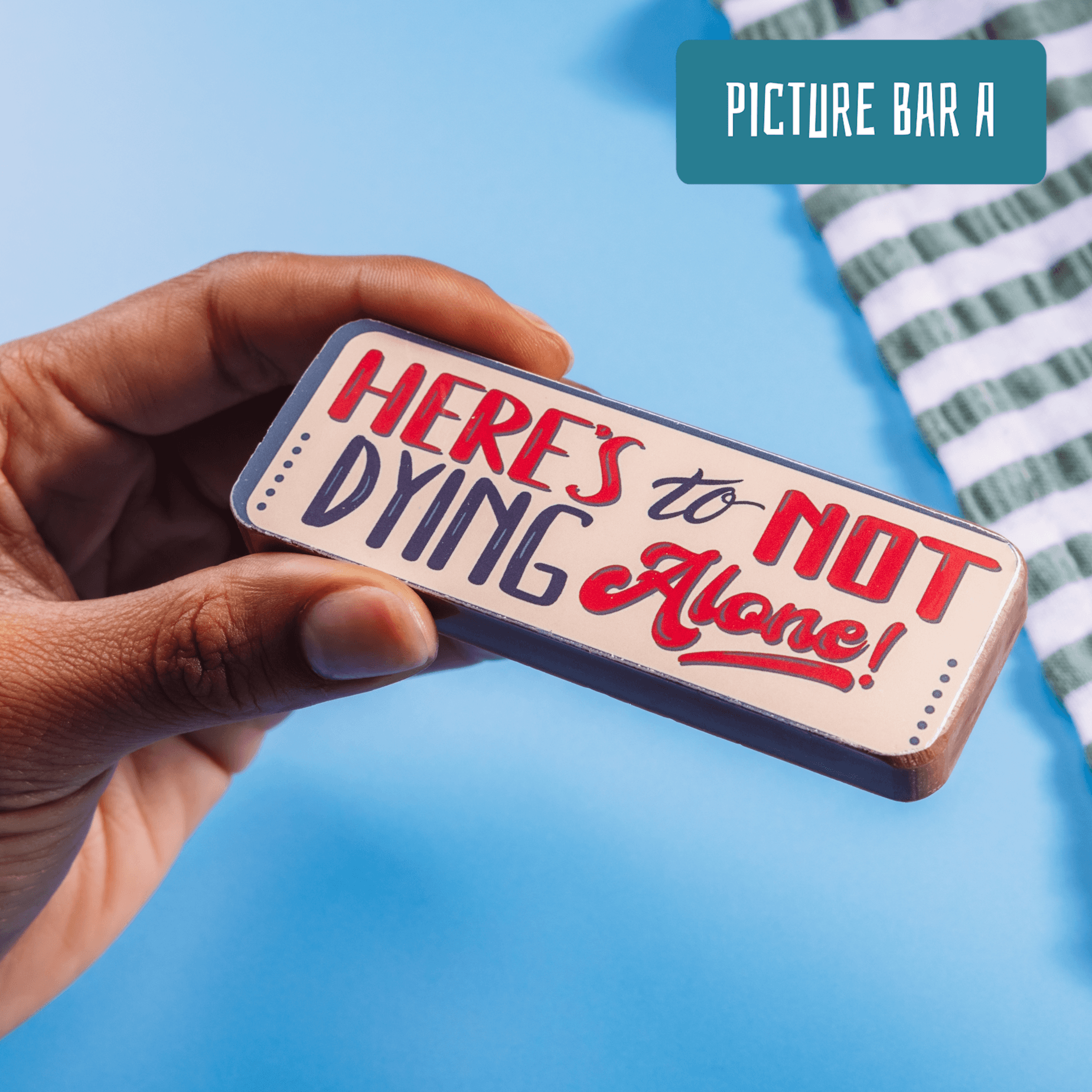 Close-up of a tongue-in-cheek chocolate bar that says “Here’s to not dying alone!” in bold, colourful lettering. From Bagstock & Bumble’s chocolates for engagement range.