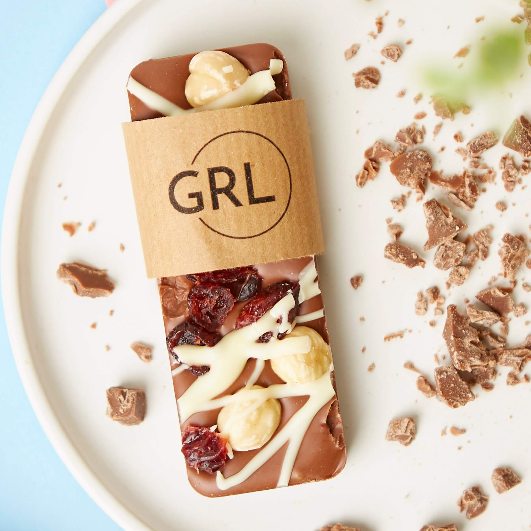 Milk chocolate bar with cranberry and hazelnuts on a plate with branded packaging.