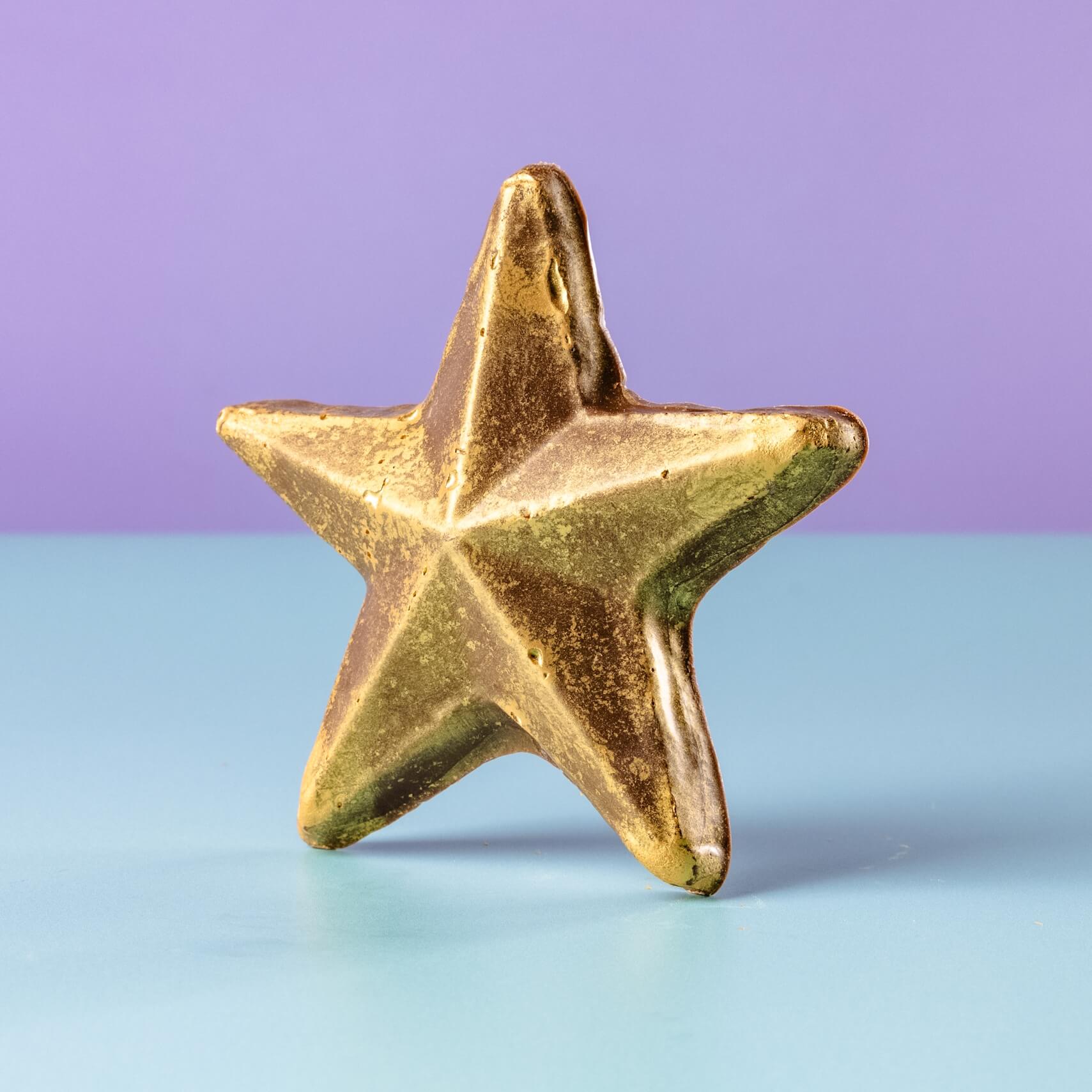A standing gold-dusted chocolate star against a pastel backdrop – the ultimate chocolate reward for good behaviour, great effort, or just showing up.