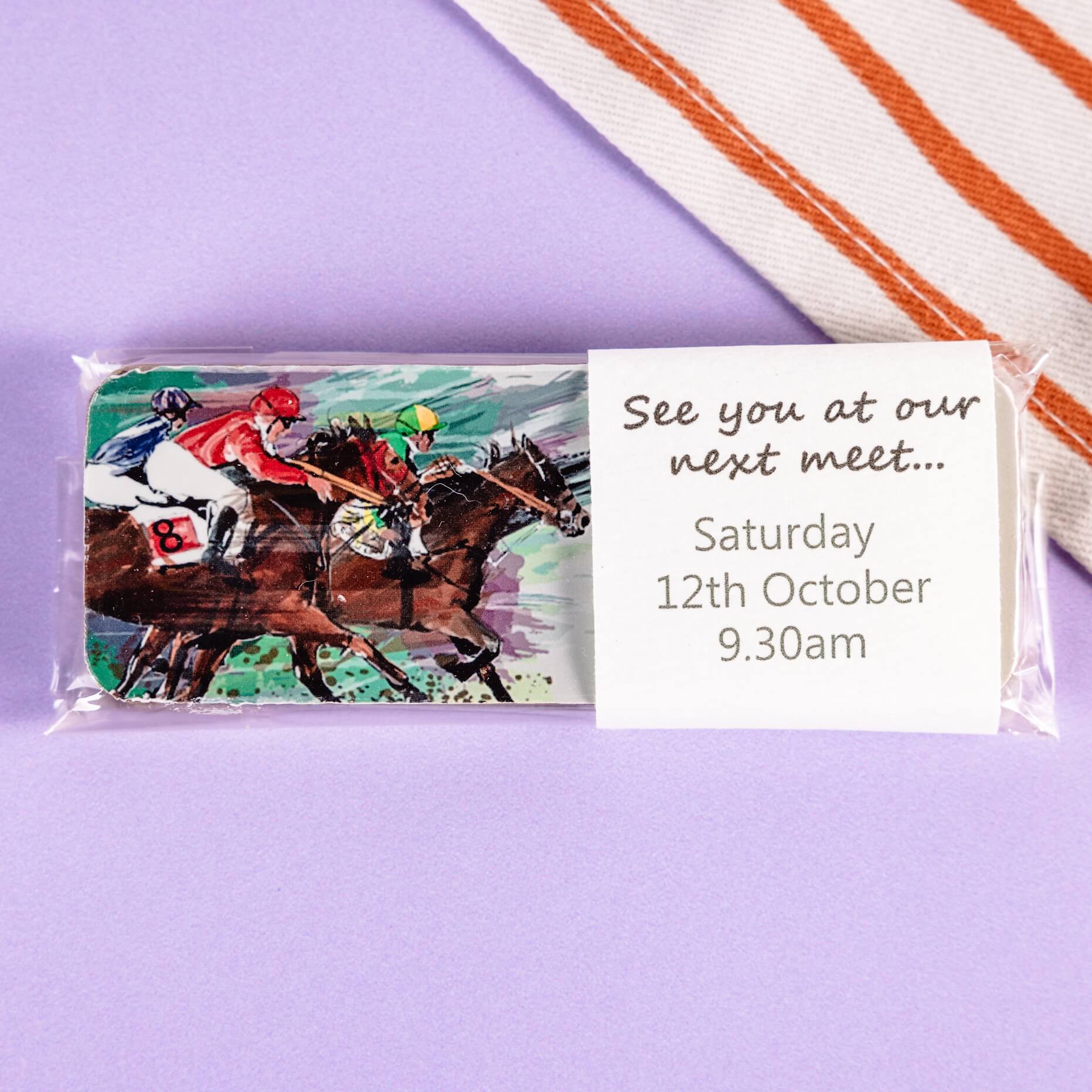 Packaged illustrated chocolate bar with horse racing design and event invitation on a purple background