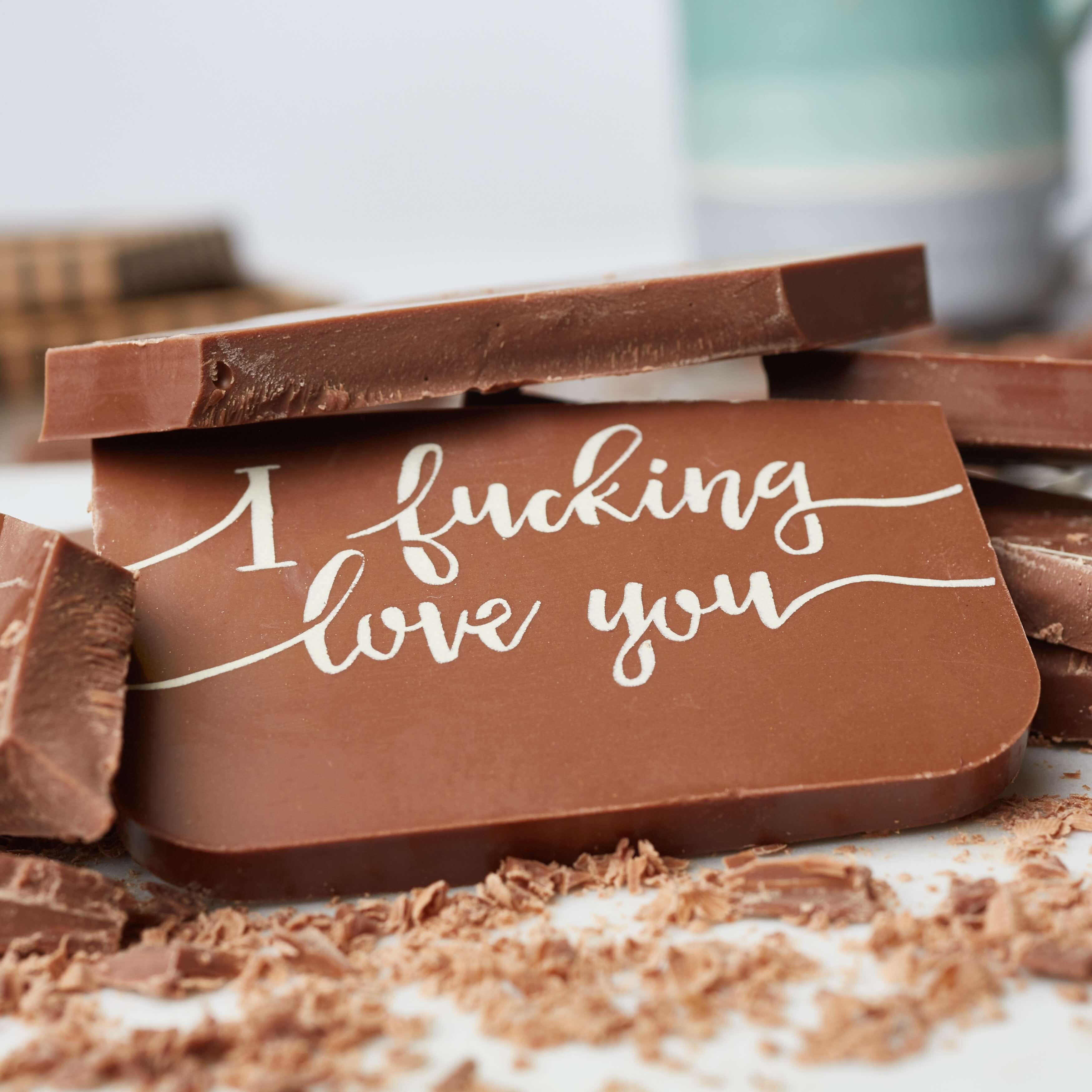 I fucking love you gift – A close-up of a chunky Belgian milk chocolate bar with the message ‘I fucking love you’, surrounded by broken pieces and chocolate shavings.