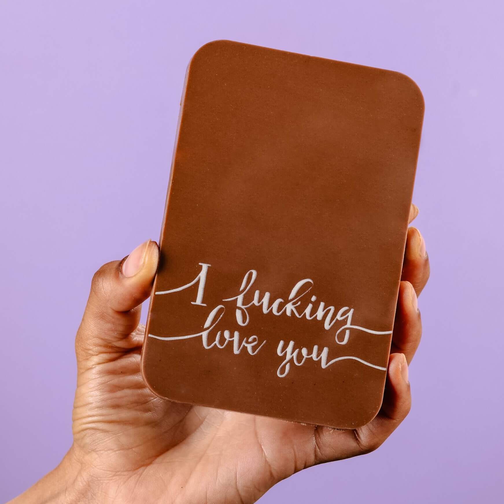 Funny and rude novelty chocolate - A close-up of a hand holding a chunky milk chocolate bar with the an ‘I fucking love you’ message written in white cocoa butter.