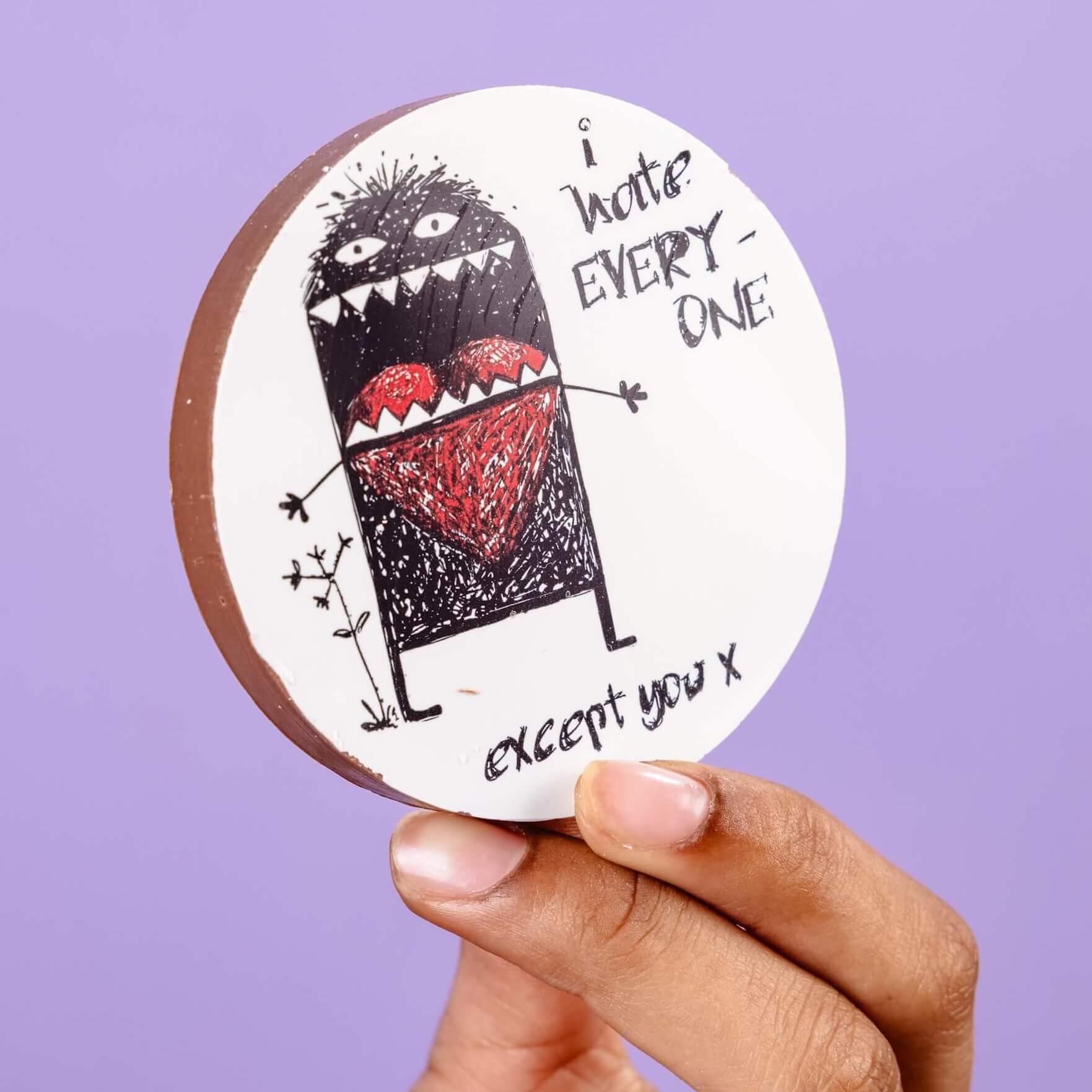 Close-up of a round chocolate disc with a printed illustration of a monster holding a red heart, and the words “I hate everyone… except you x” – the perfect I hate everyone gift for someone who’s won your black little heart.