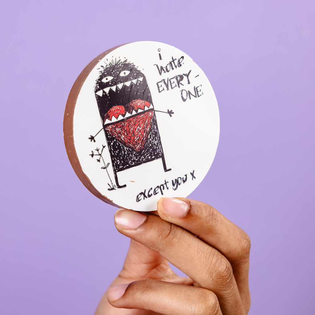 Our funny Valentine's Day gift.  A hand holds up a chunky chocolate disc, 8cm in diameter, with a picture of a cartoon monster with a heart in his mouth and the caption 'I hate everyone except you'.