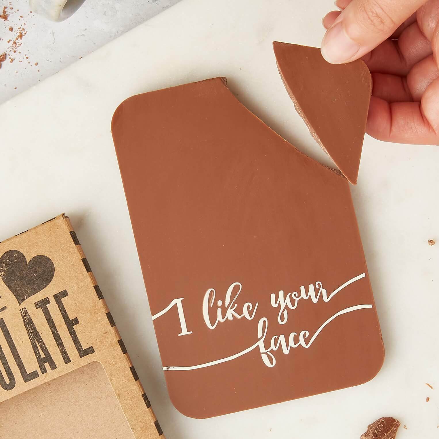 A hand breaking a piece off a milk chocolate bar with the message “I like your face” – a playful chocolate gift for couples who prefer snacks over sonnets.