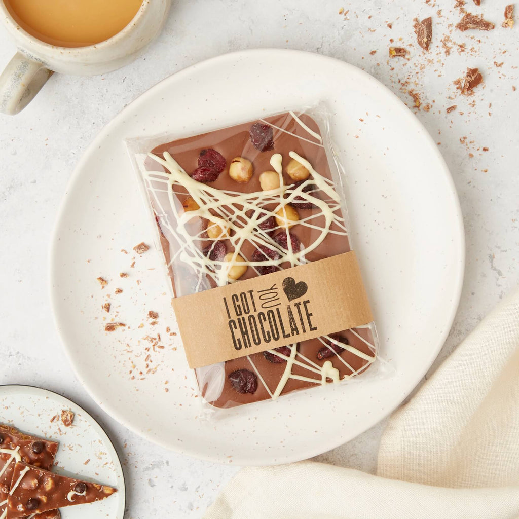A wrapped chocolate slab featuring chocolate with hazelnut and cranberry toppings, finished with a kraft paper band that reads “I got you chocolate”.