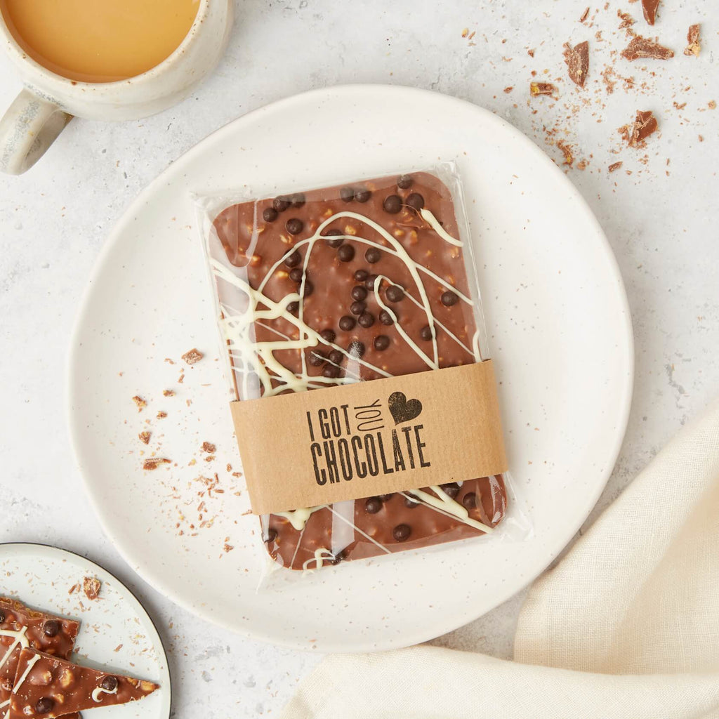 A packaged bar of chocolate honeycomb topped with a drizzle of white chocolate and crispy dark chocolate balls, wrapped in a kraft sleeve that reads “I got you chocolate”.