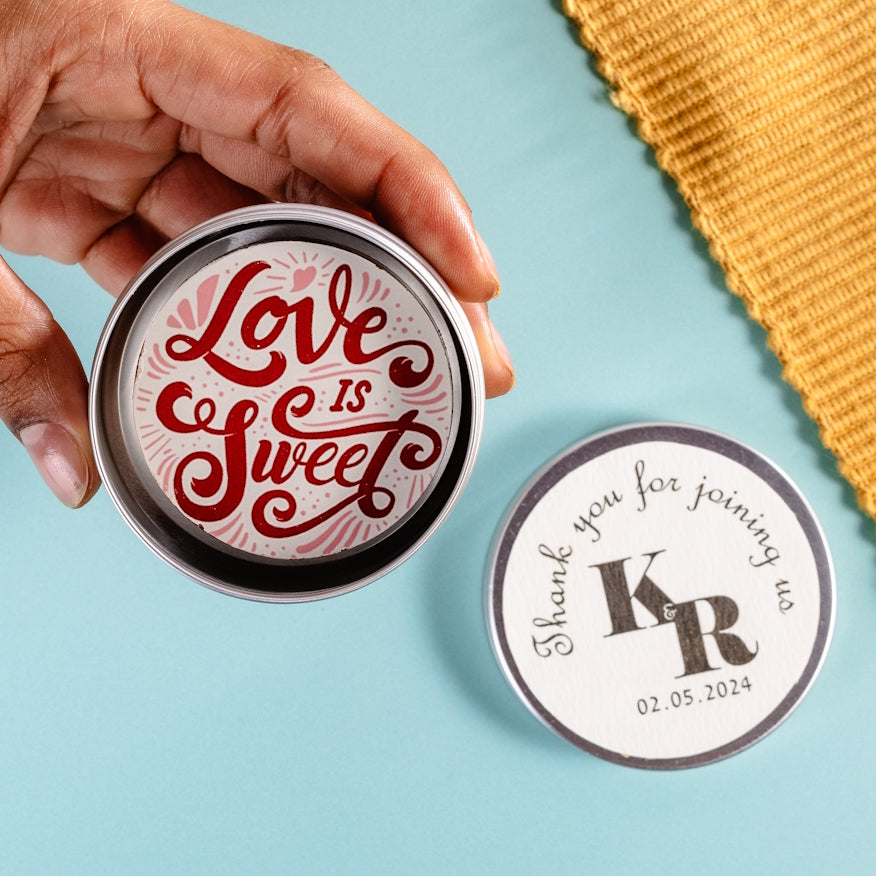Hand holding a small round tin with a 'Love is Sweet' chocolate inside and, shown behind, the lid is personalised with a sticker