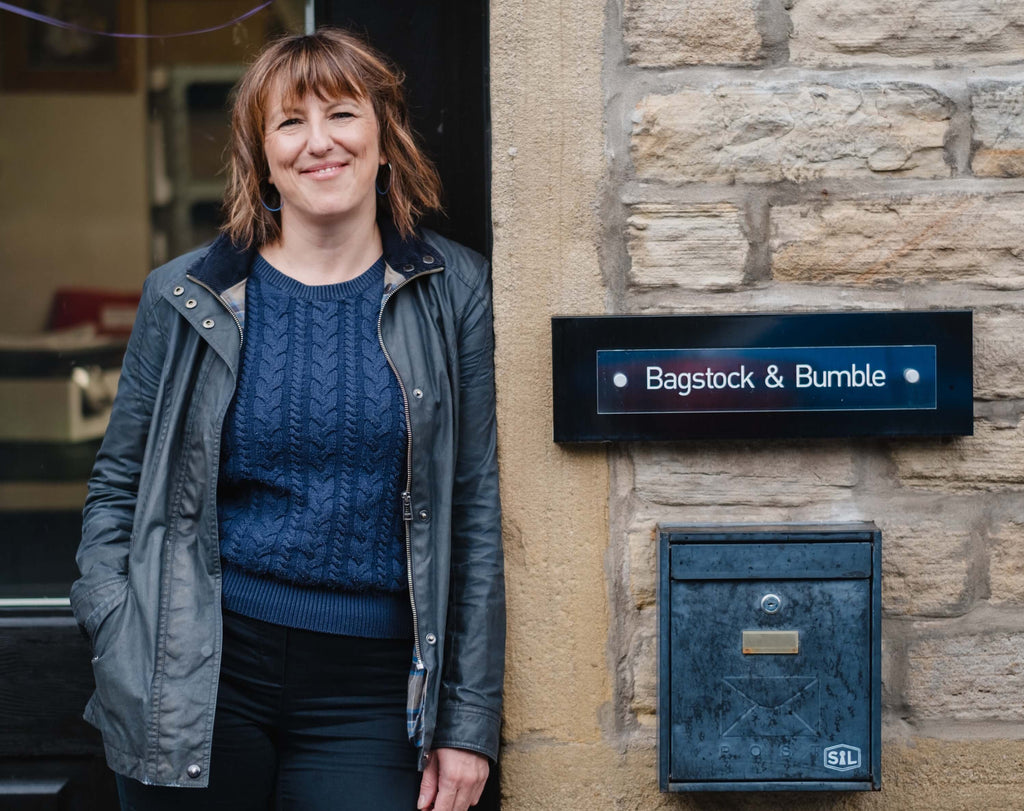 Katherine the owner standing in front of a stone building with a sign that reads 'Bagstock & Bumble'.