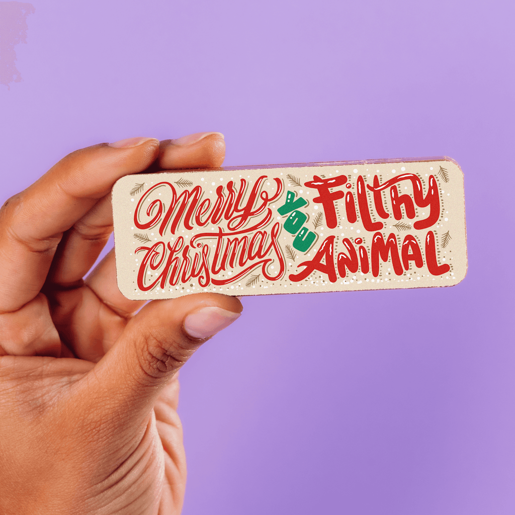 Close-up of a hand holding a decorated milk chocolate bar with the words "Merry Christmas you filthy animal" in a festive font