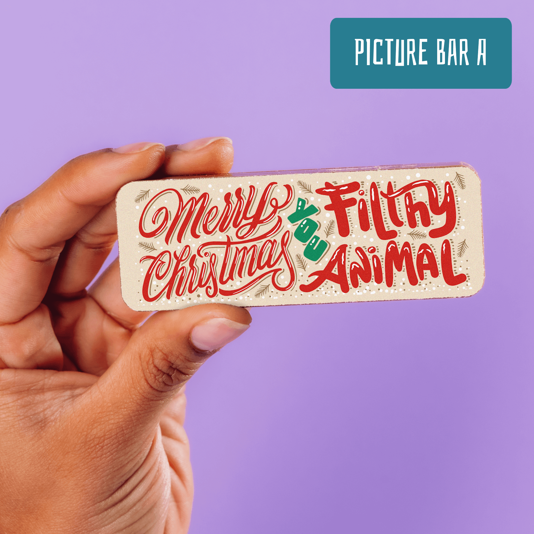 Close-up of a hand holding a decorated milk chocolate bar with the words "Merry Christmas you filthy animal" in a festive font