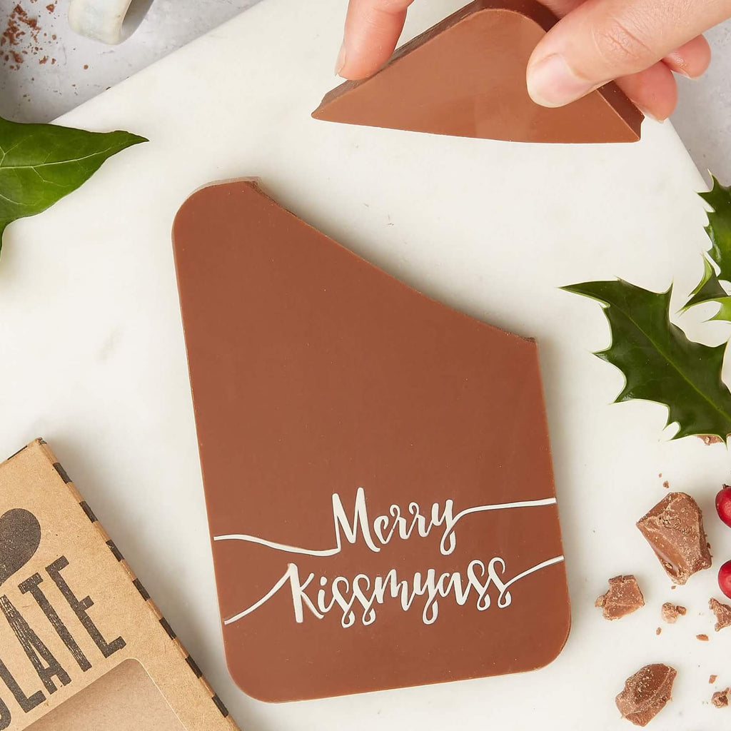 A chunky milk chocolate bar with  cheeky “Merry Kissmyass” message, being snapped apart – a funny christmas chocolate gift with bite.